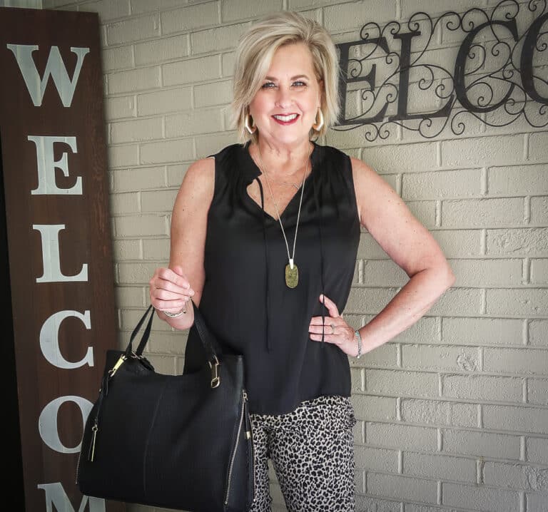 Fashion Blogger 50 Is Not Old is wearing a black smocked tank top, a pair of animal print pants, and a black lambskin tote