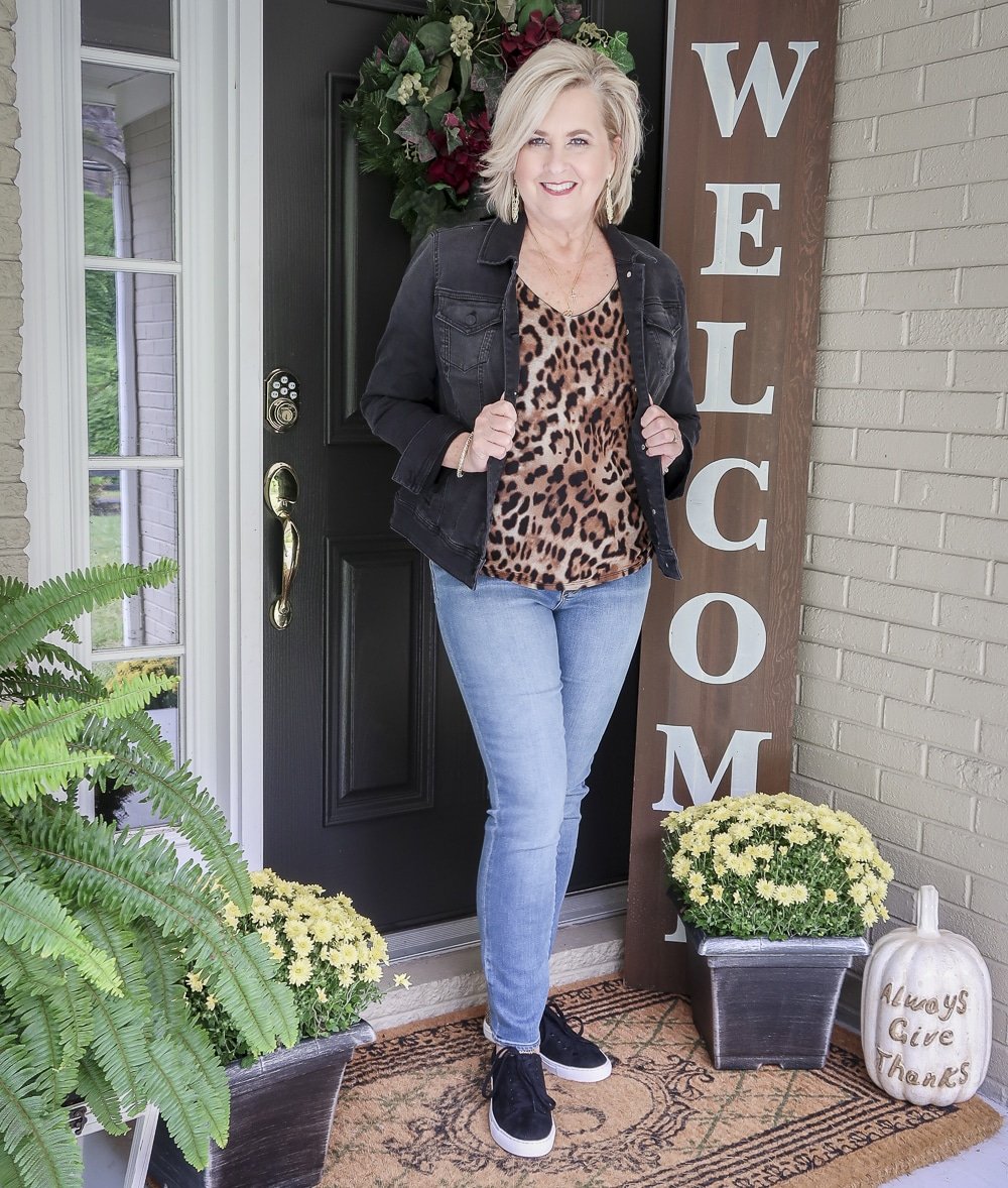 Fashion Blogger 50 Is Not Old in a fall try-on session wearing a black denim jacket, a leopard tank top, and ankle jeans from Chicos, and black leopard sneakers from J Crew