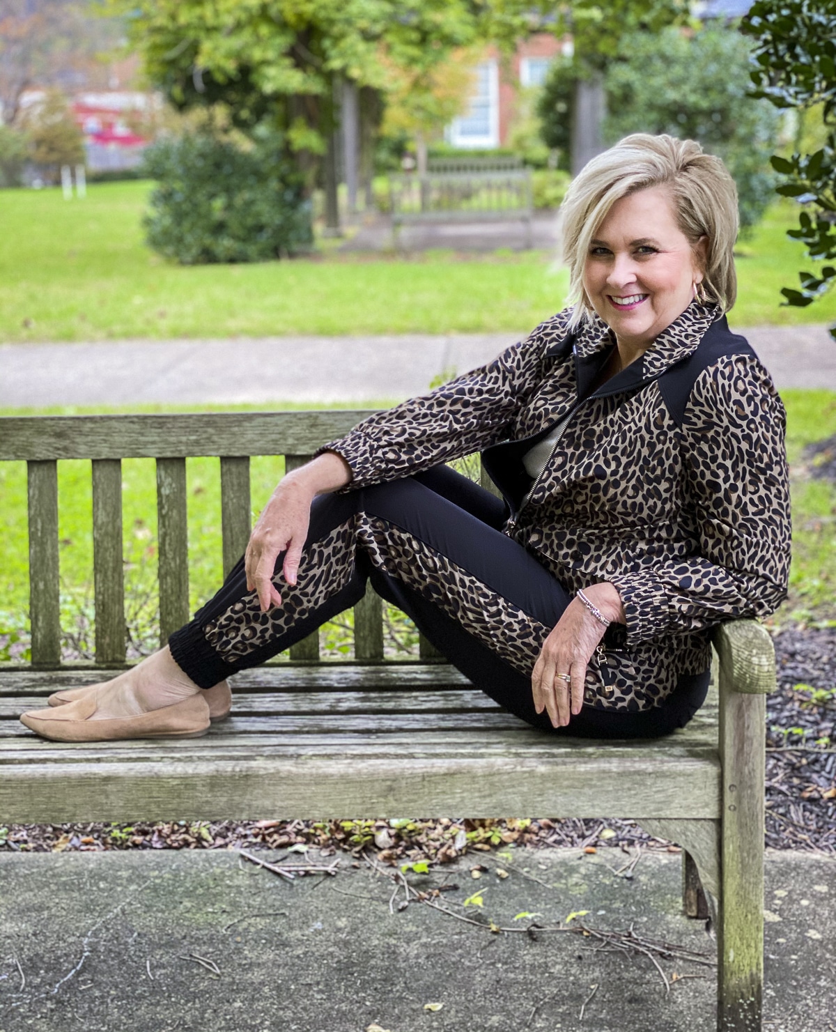 Fashion Blogger 50 Is Not Old is sitting on a bench in a Cheetah print jacket and joggers from Chicos
