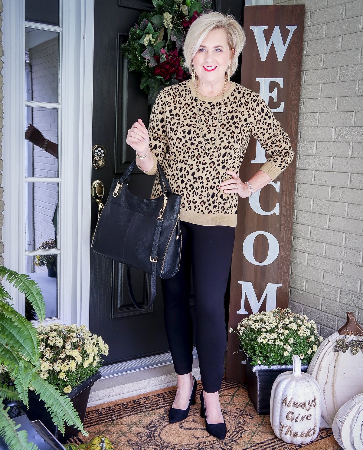 Fashion Blogger 50 Is Not Old is styling a leopard print sweater, black SPANX pants, and carrying a black Vince Camuto handbag.