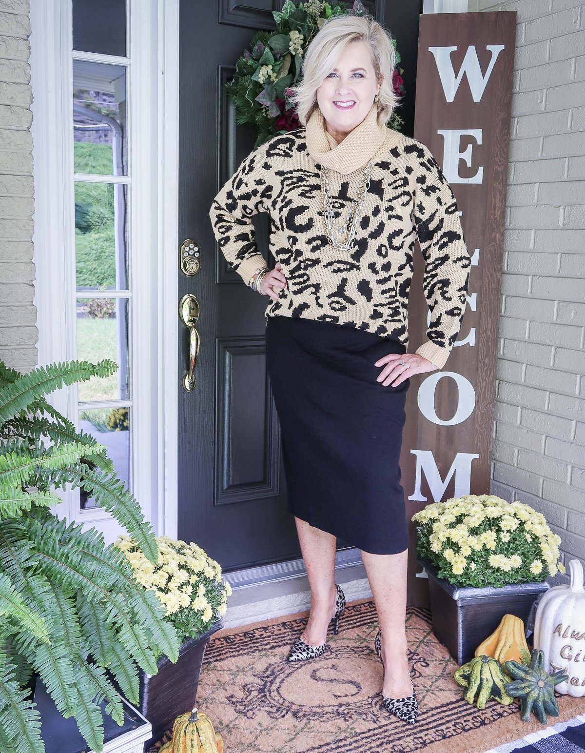 Fashion Blogger 50 Is Not Old is wearing a leopard print cowl neck sweater, a black sweater skirt, gold jewelry, and high heel shoes