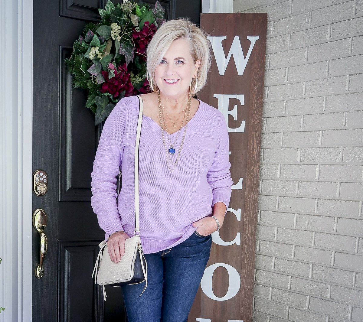 Fashion Blogger 50 Is Not Old is wearing a gorgeous purple v-neck sweater with a Vince Camuto Crossbody handbag