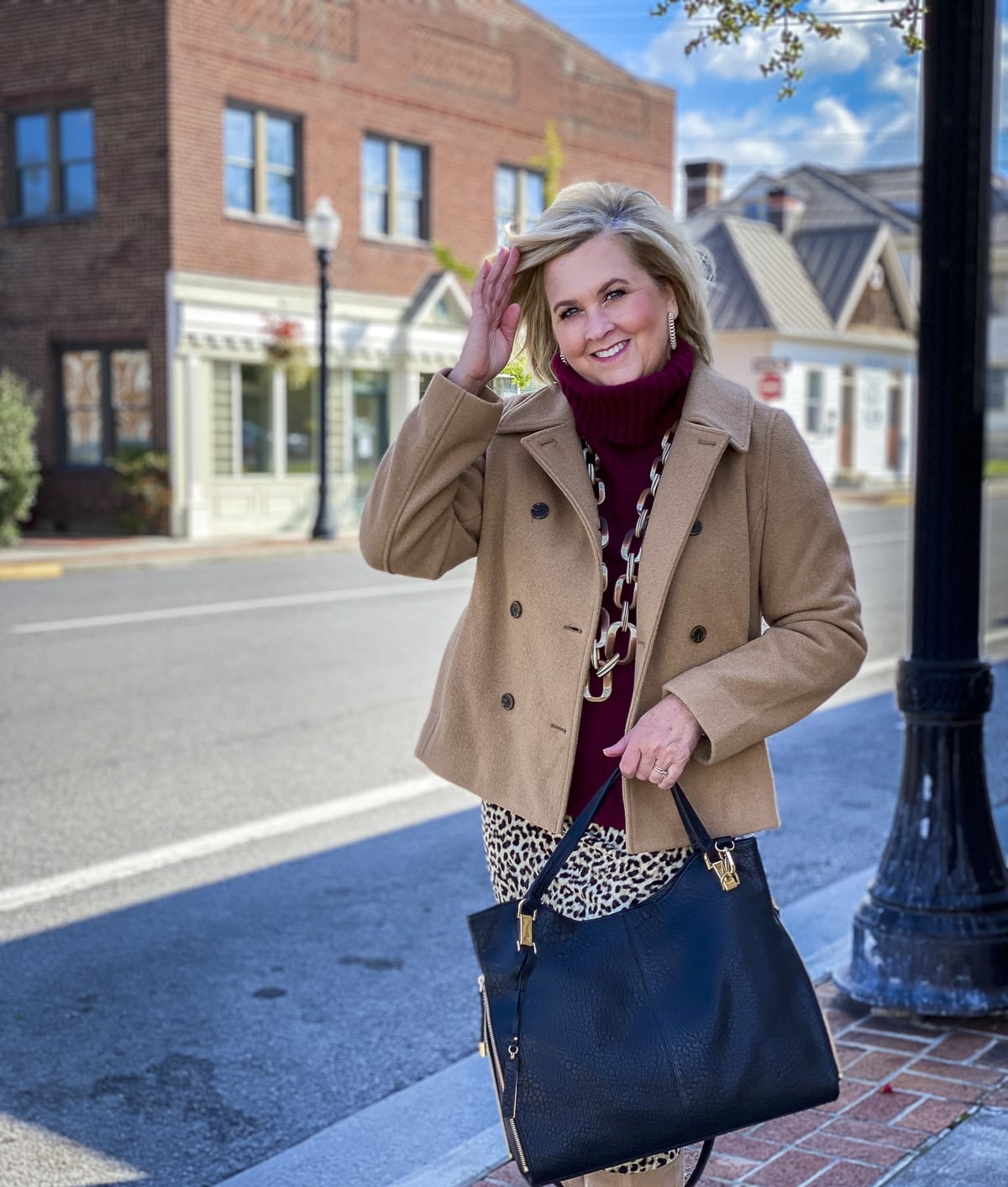 Fashion Blogger 50 Is Not Old is wearing a maroon turtleneck sweater, a camel peacoat, and carrying a black handbag