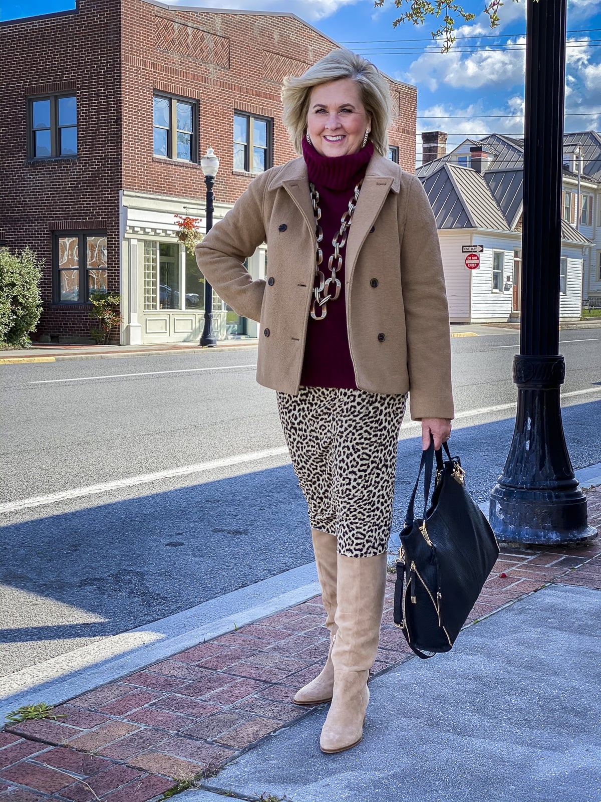 Fashion Blogger 50 Is Not Old is wearing a maroon turtleneck sweater, a camel peacoat, a leopard tube skirt, suede knee boots, and carrying a black handbag
