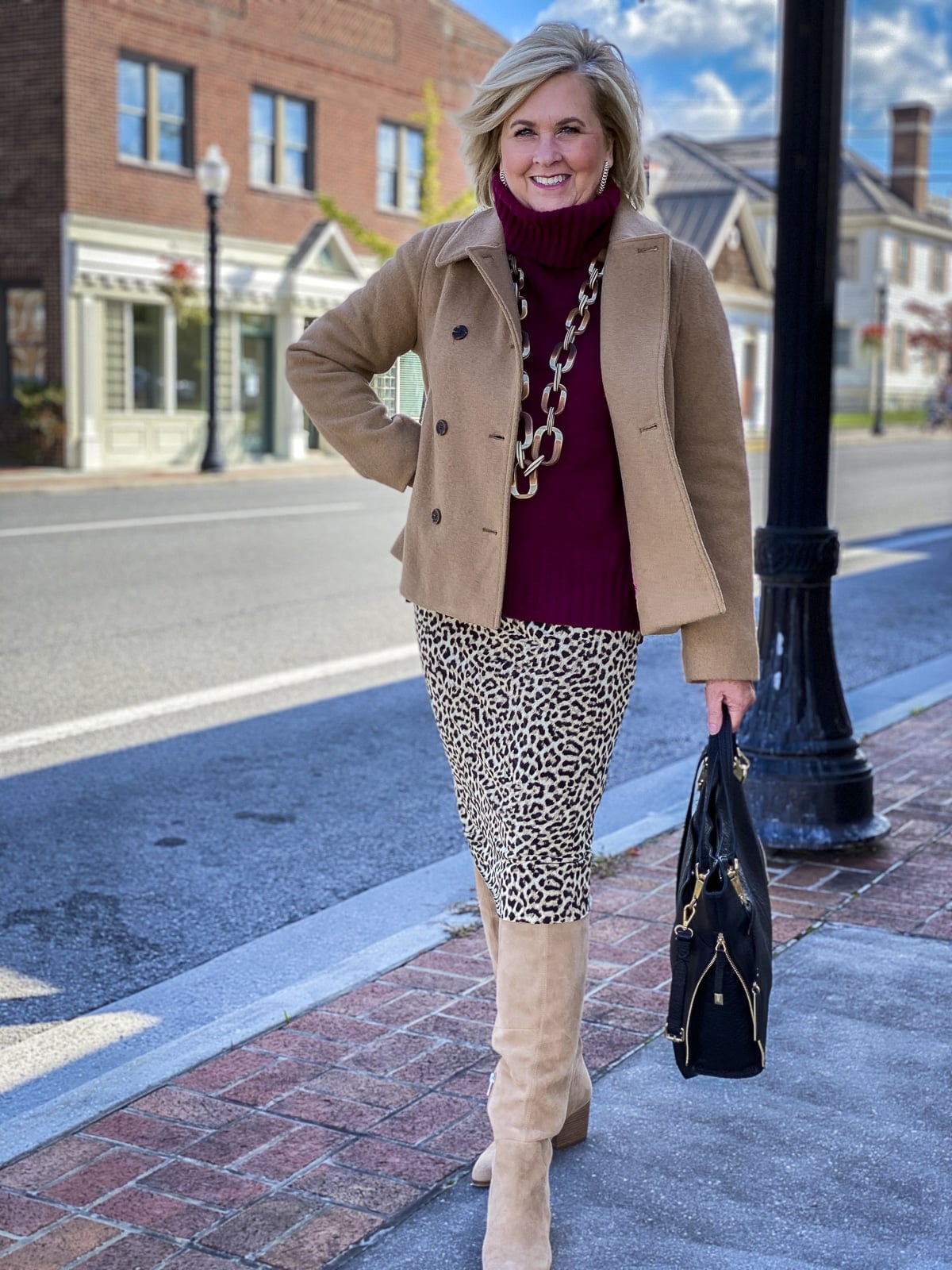 Fashion Blogger 50 Is Not Old is wearing a maroon turtleneck sweater, a camel peacoat, a leopard tube skirt, and suede knee boots