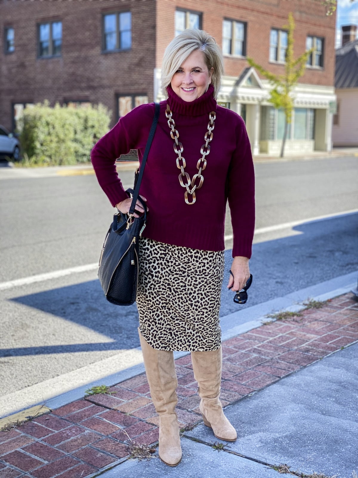 Fashion Blogger 50 Is Not Old is wearing a maroon turtleneck sweater, a leopard tube skirt, suede knee boots, and carrying a black handbag by Vince Camuto