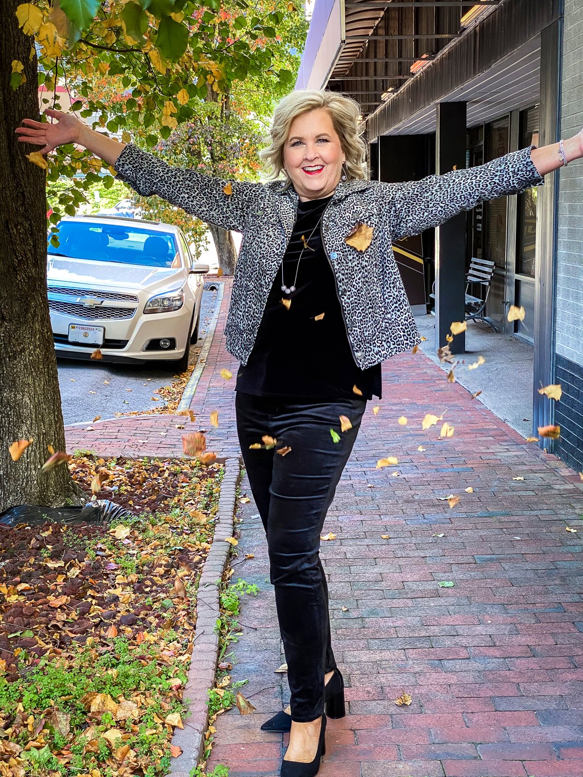Fashion Blogger 50 Is Not Old is showered with leaves in a black velvet tank top, an animal print jacket, and black velvet jeggings from Chico's