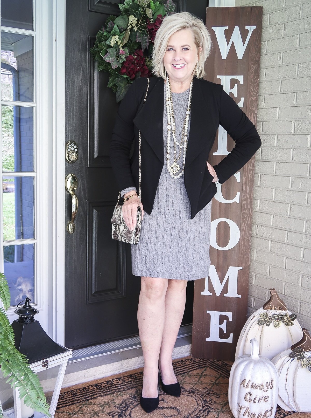 Fashion Blogger 50 Is Not Old is wearing a gray cable-knit sweater dress with a black blazer, black heels, a snakeskin handbag, and a multi-strand pearl necklace