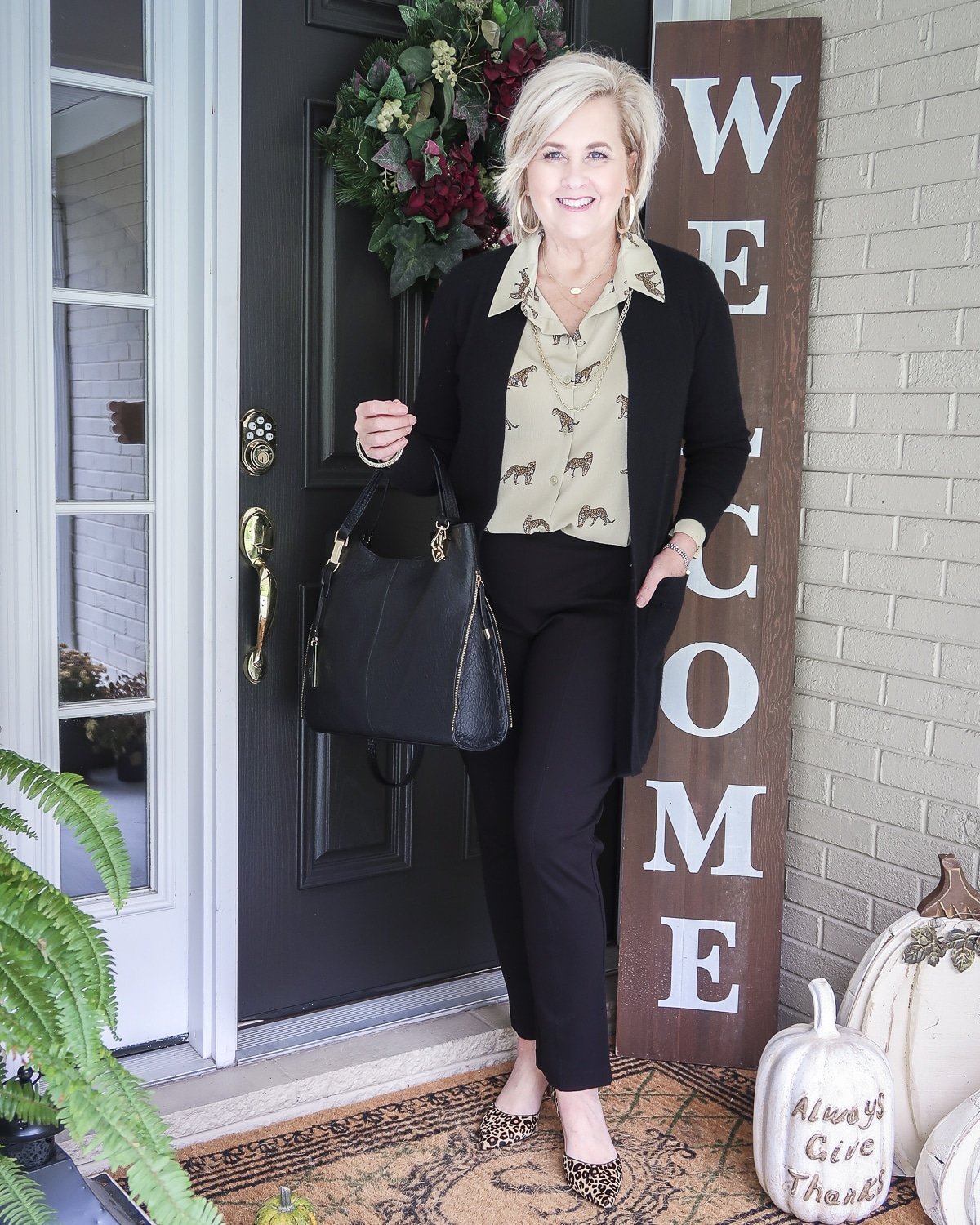 Fashion Blogger 50 Is Not Old is wearing a leopard print button down blouse with a black cardigan, carrying a black handbag, and wearing black ankle pants with leopard print heels