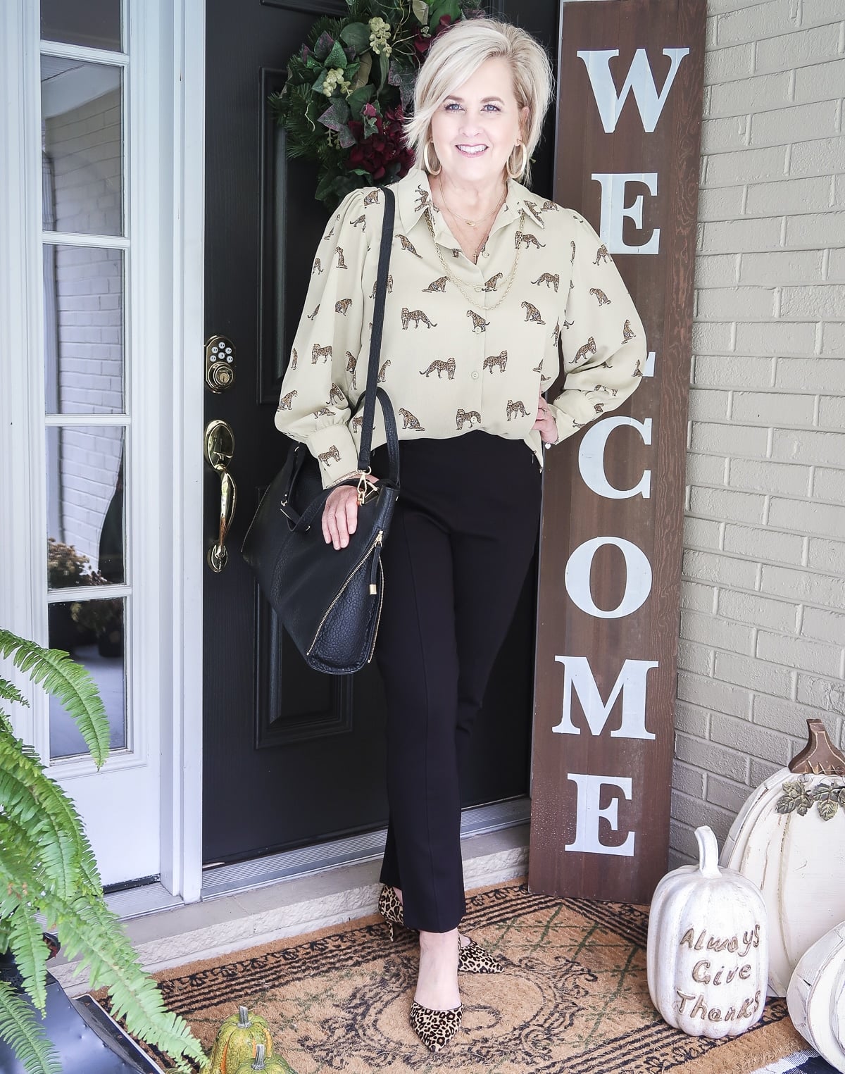 Fashion Blogger 50 Is Not Old is wearing a leopard print button down blouse with a black handbag and black ankle pants with leopard print heels