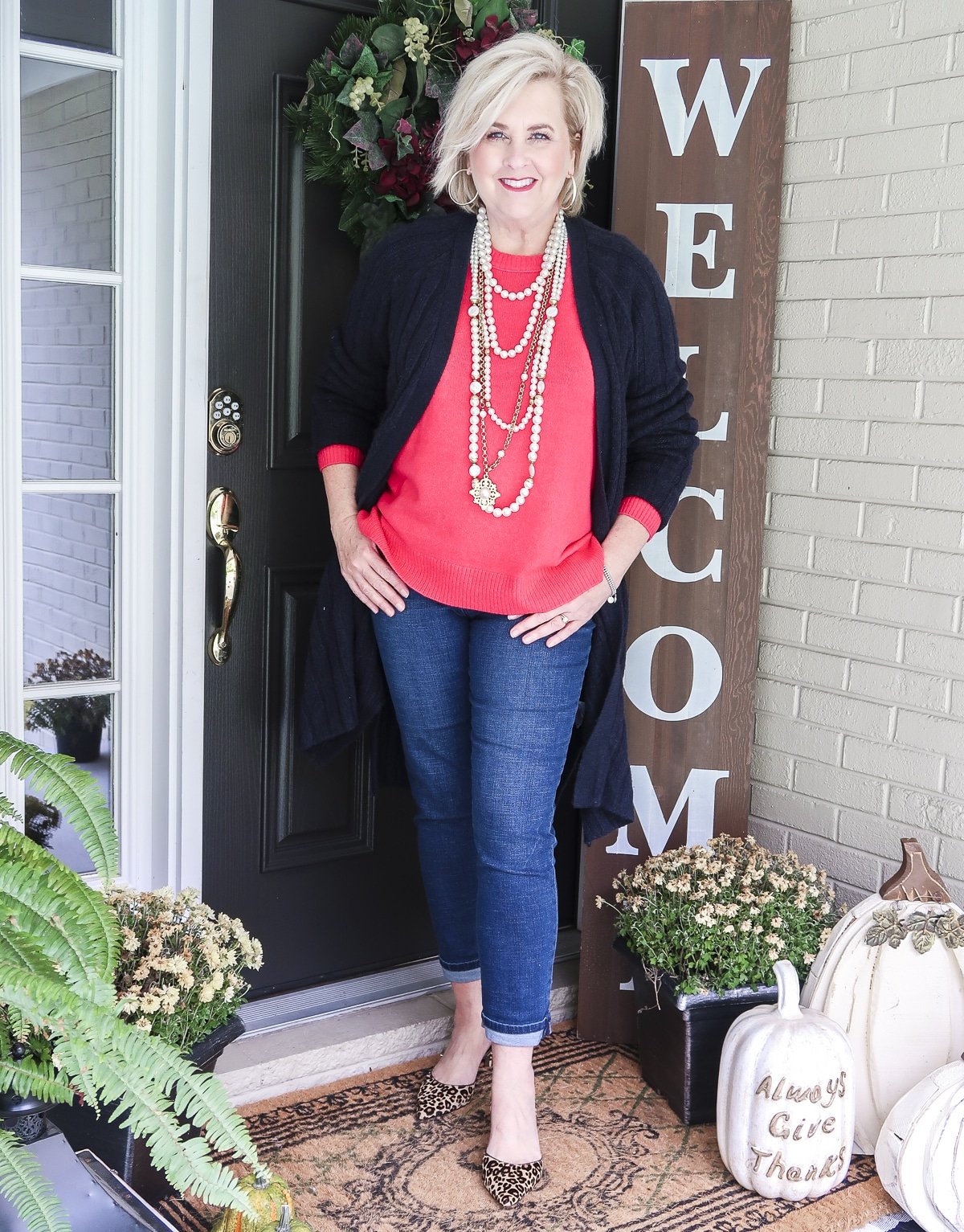 Fashion Blogger 50 Is Not Old is wearing a bright pink sweater lots of pearls necklaces, ankle jeans, and leopard print heels