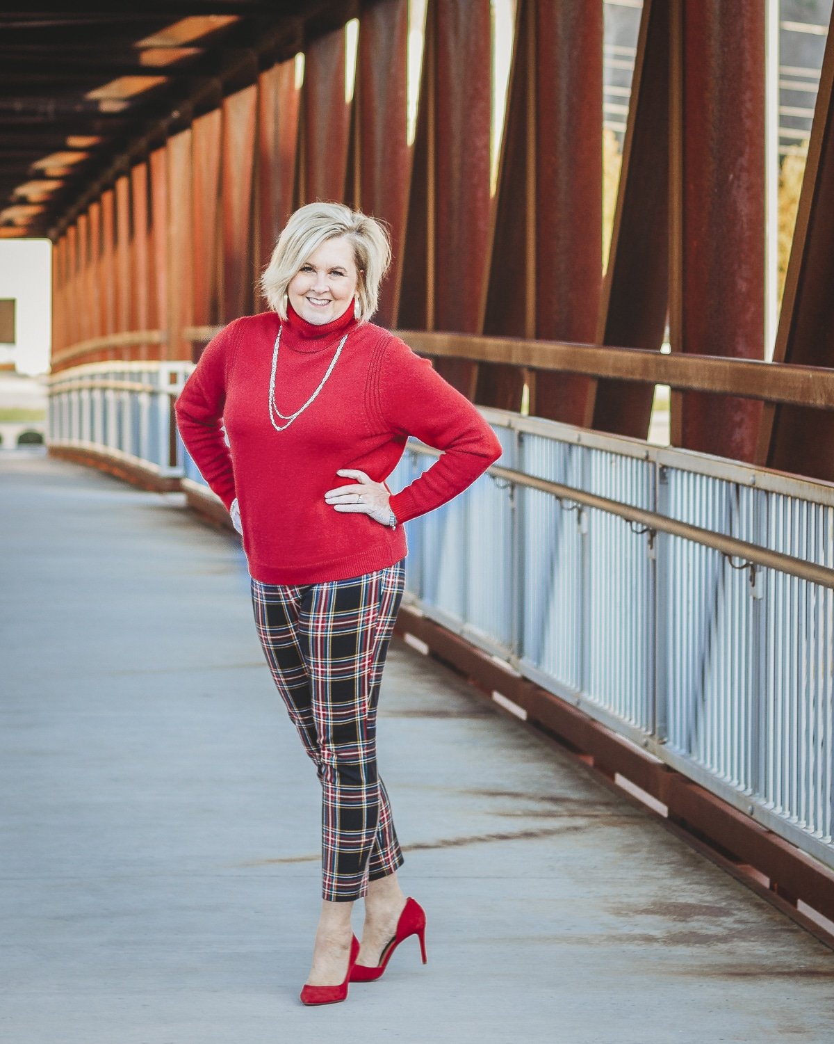 Fashion Blogger 50 Is Not Old is looking festive in this red turtleneck sweater, gold jewelry, plaid pants, and red heels