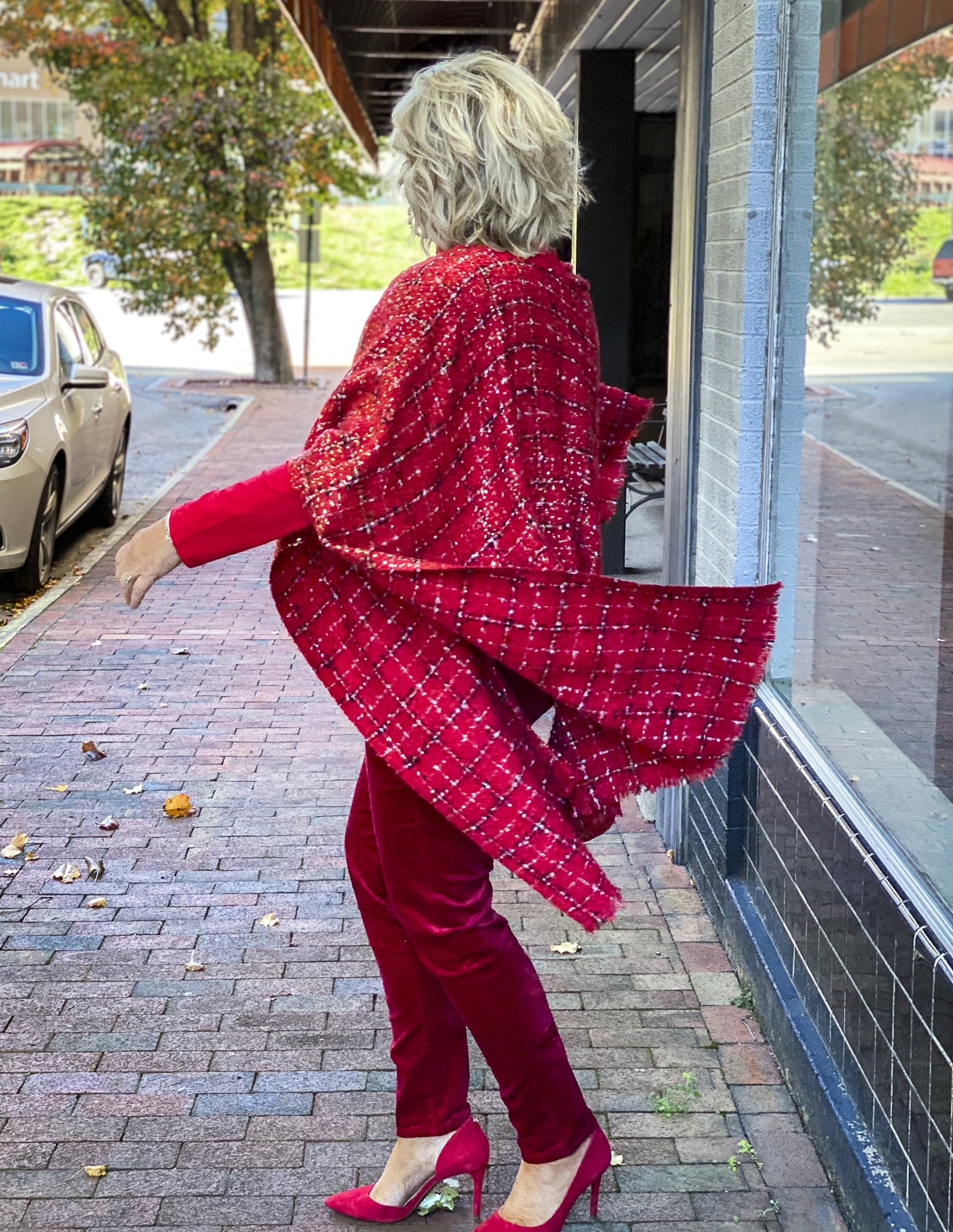 Fashion Blogger 50 Is Not Old is wearing a monochromatic red outfit with a red ruana blowing in the wind