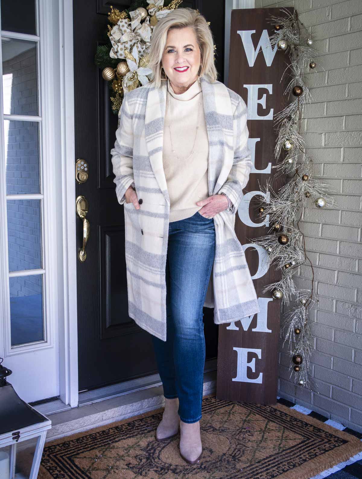 Fashion Blogger 50 Is Not Old is wearing a funnel mock neck neutral sweater, a long plaid double breasted coat, straight leg jeans, and ankle boots