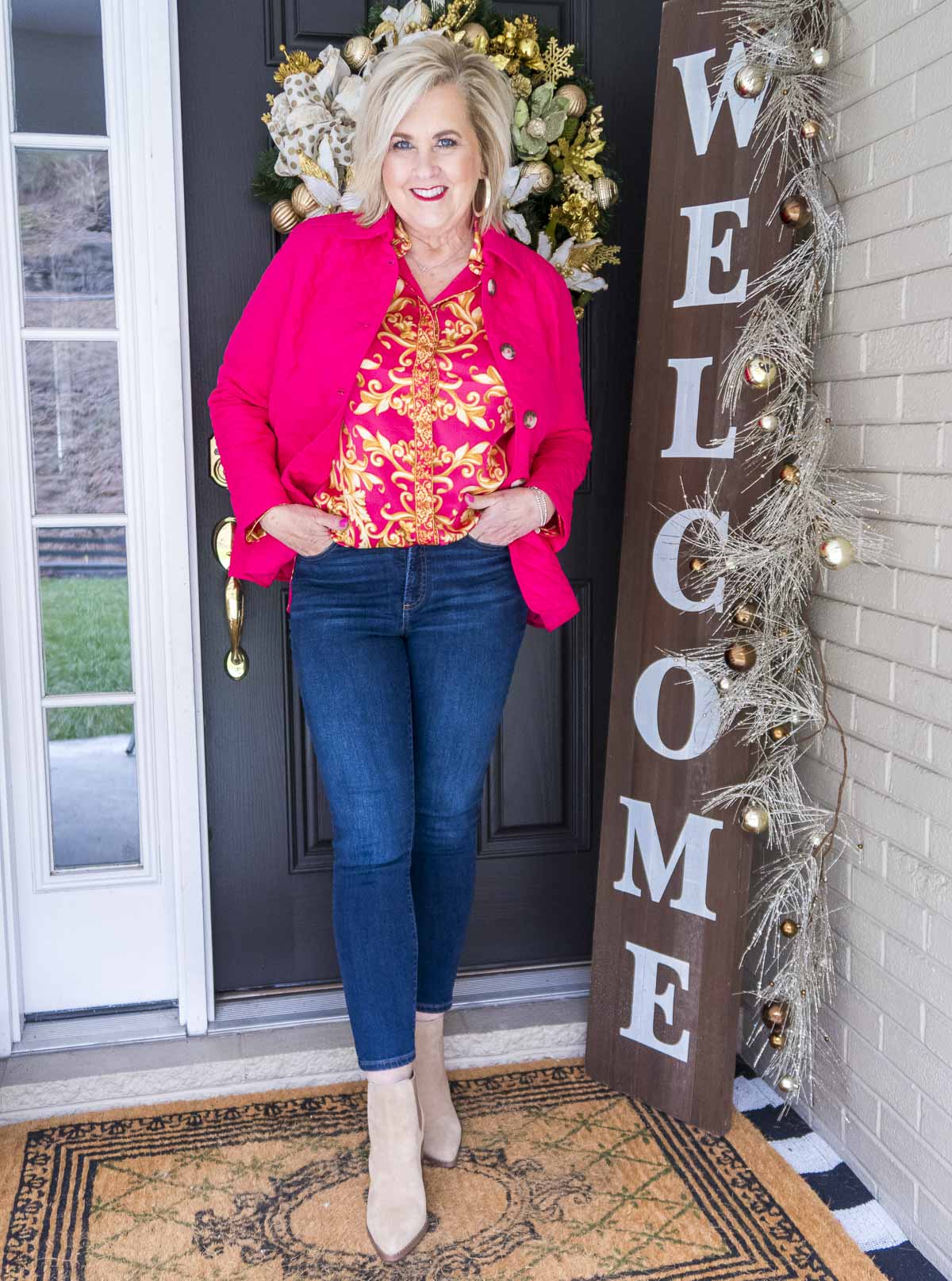 Fashion Blogger 50 Is Not Old is wearing a bright and bold colored pink jacket and scroll print blouse with dark wash skinny ankle jeans and neutral colored booties