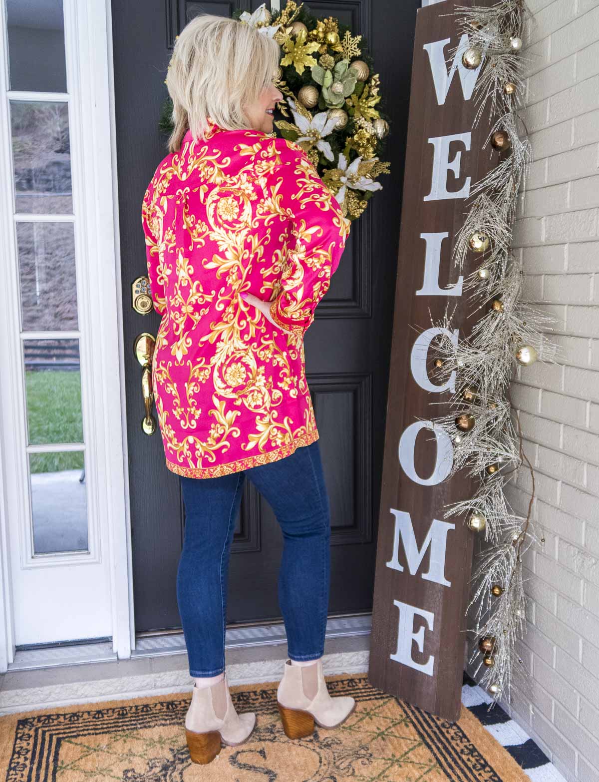Fashion Blogger 50 Is Not Old is showing the back of a scroll print blouse with dark wash skinny ankle jeans and neutral colored booties