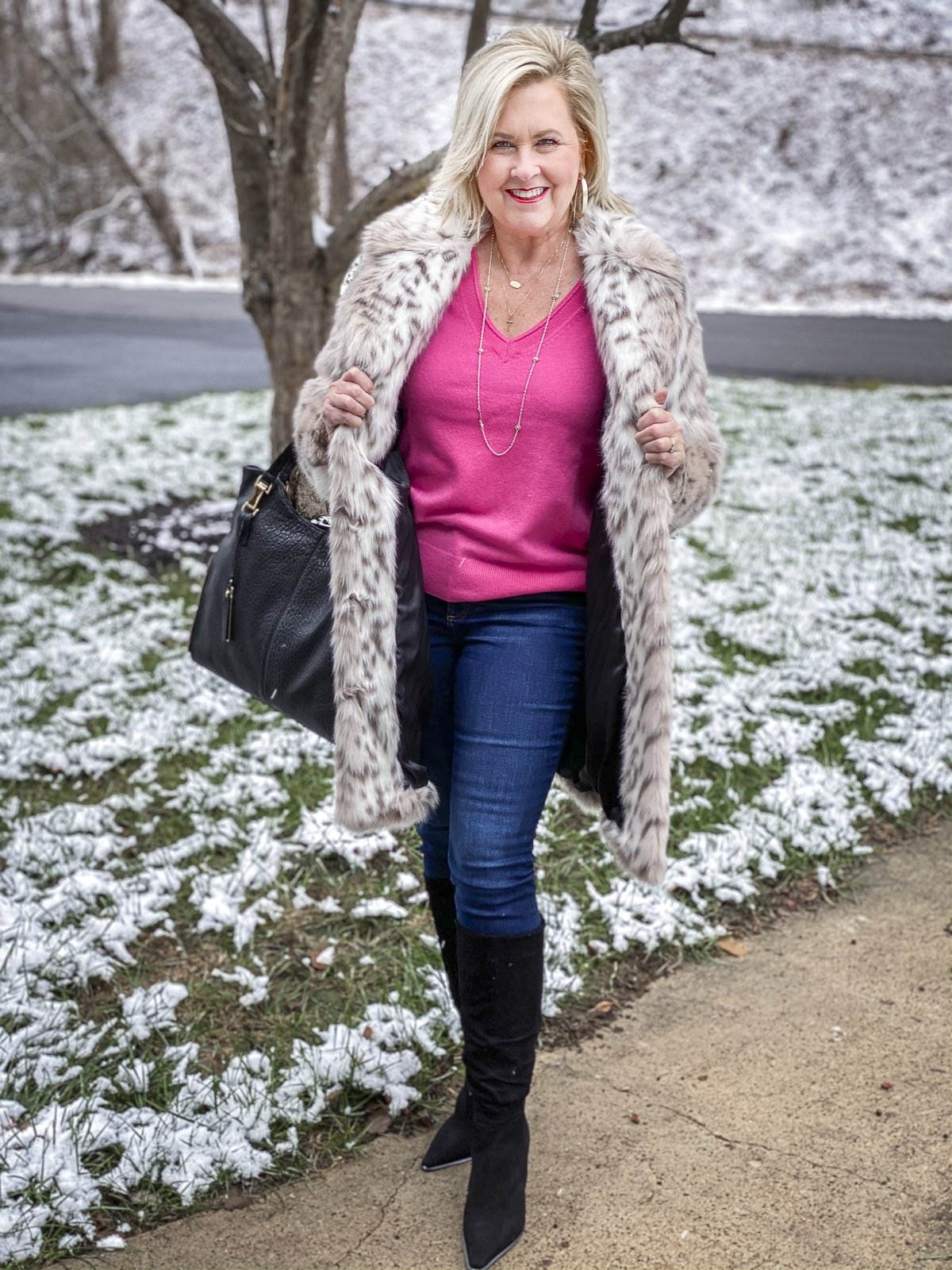 FASHION BLOGGER 50 IS NOT OLD is wearing a faux fur coat by Karl Lagerfeld and showing a bright pink v-neck cashmere sweater, skinny jeans, and black suede boots