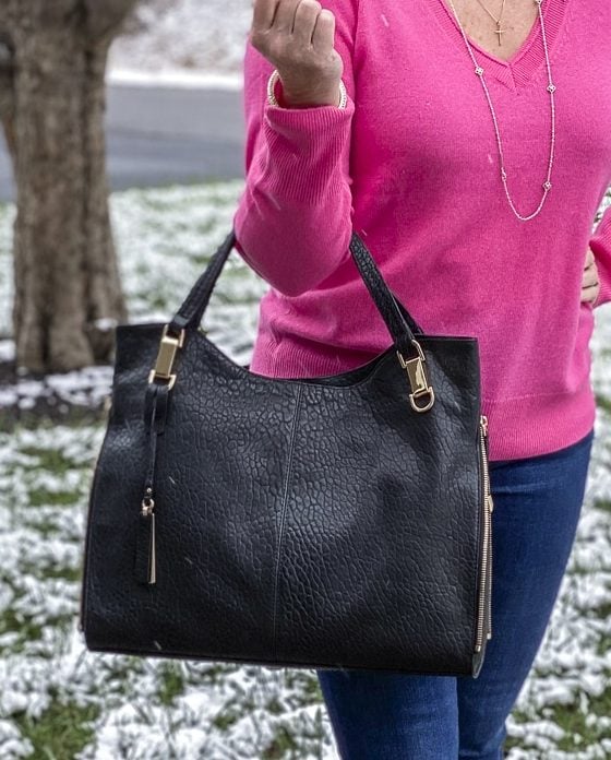 FASHION BLOGGER 50 IS NOT OLD is wearing a bright pink v-neck cashmere sweater and carrying a black handbag