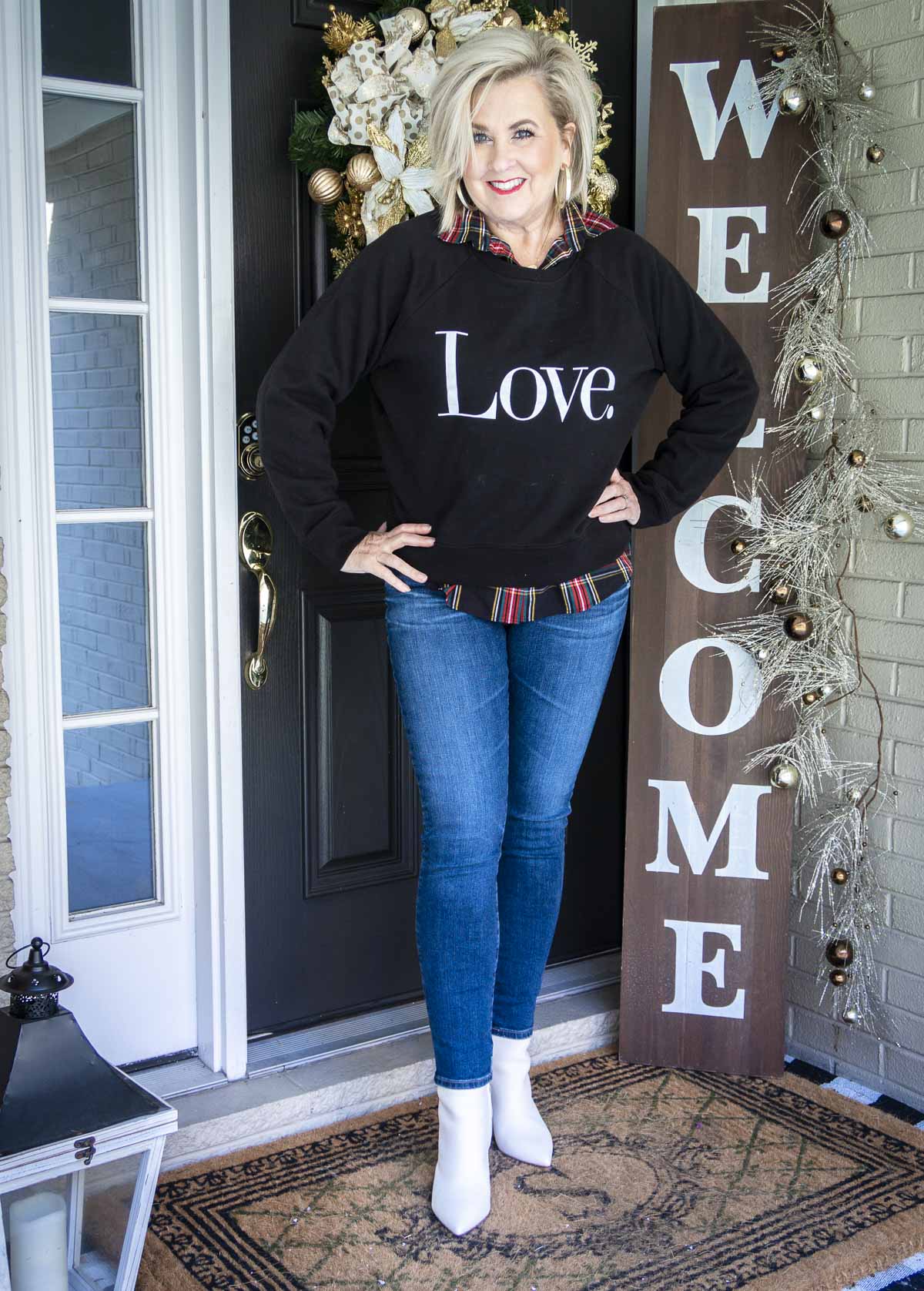 Fashion Blogger 50 Is Not Old is wearing a black sweatshirt that says LOVE, a pair of skinny jeans and white booties