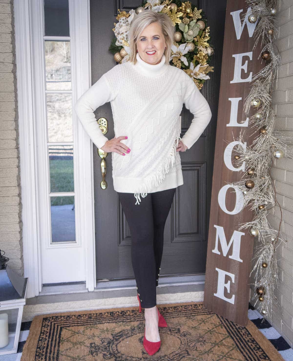 Fashion Blogger 50 Is Not Old is styling a Ecru sweater with fringe, a pair of black snap leggings, and red suede pumps