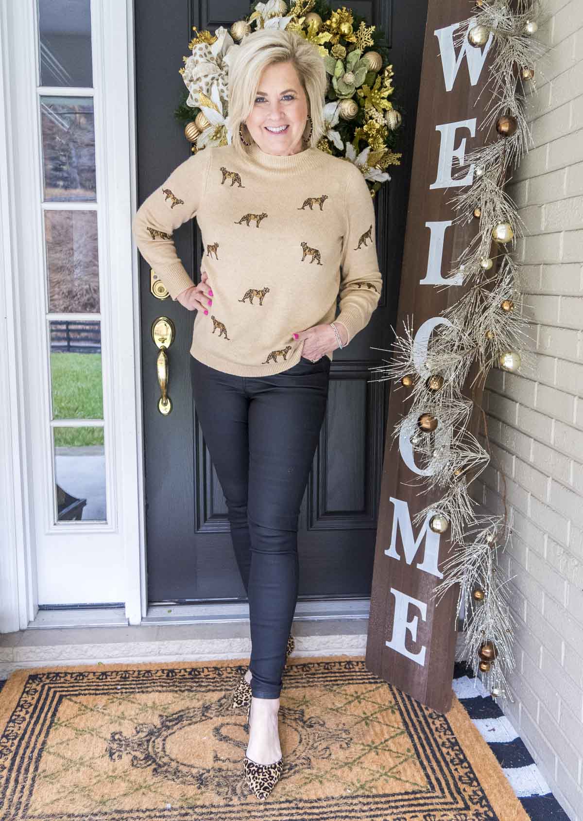 Fashion Blogger 50 Is Not Old is wearing a cashmere sweater with cheetahs embroidered on it, a pair of black coated jeans, and leopard print heels