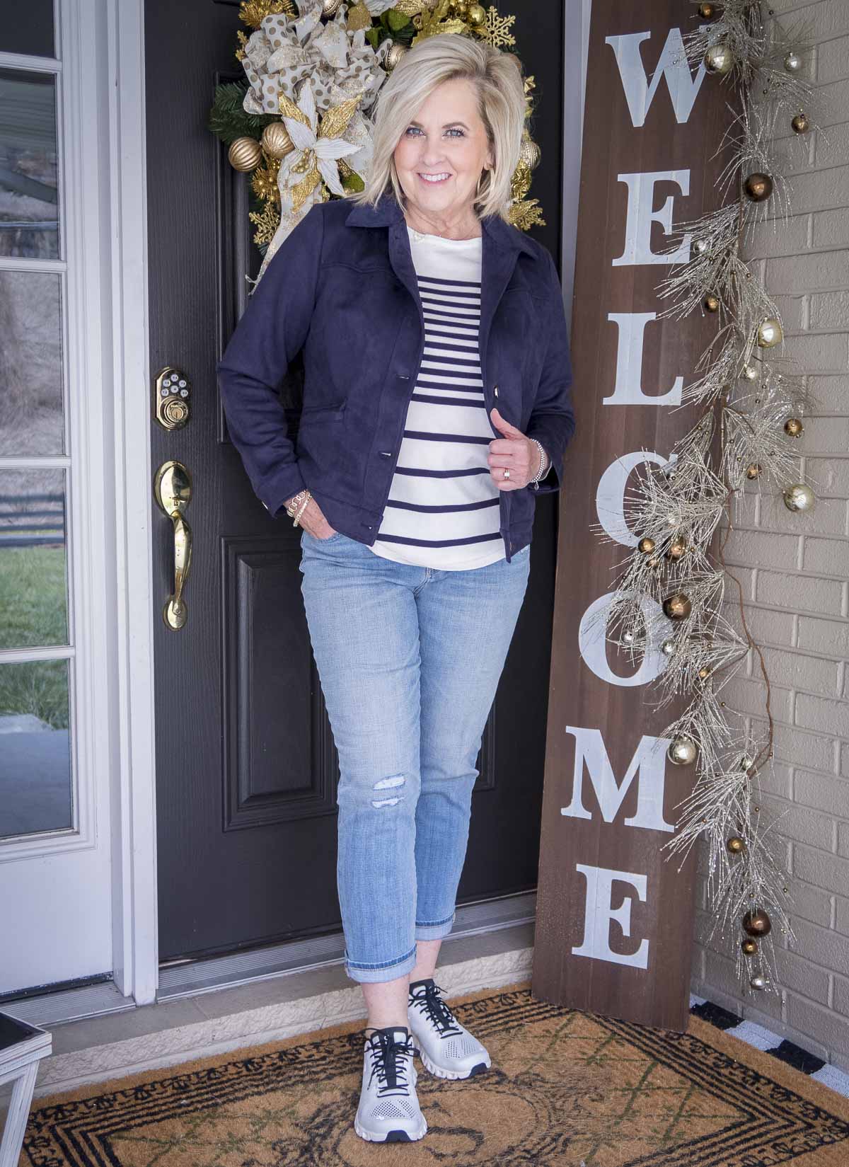 Fashion Blogger 50 Is Not Old is wearing a striped sweater with a navy faux suede jacket, light wash jeans and On Cloud sneakers