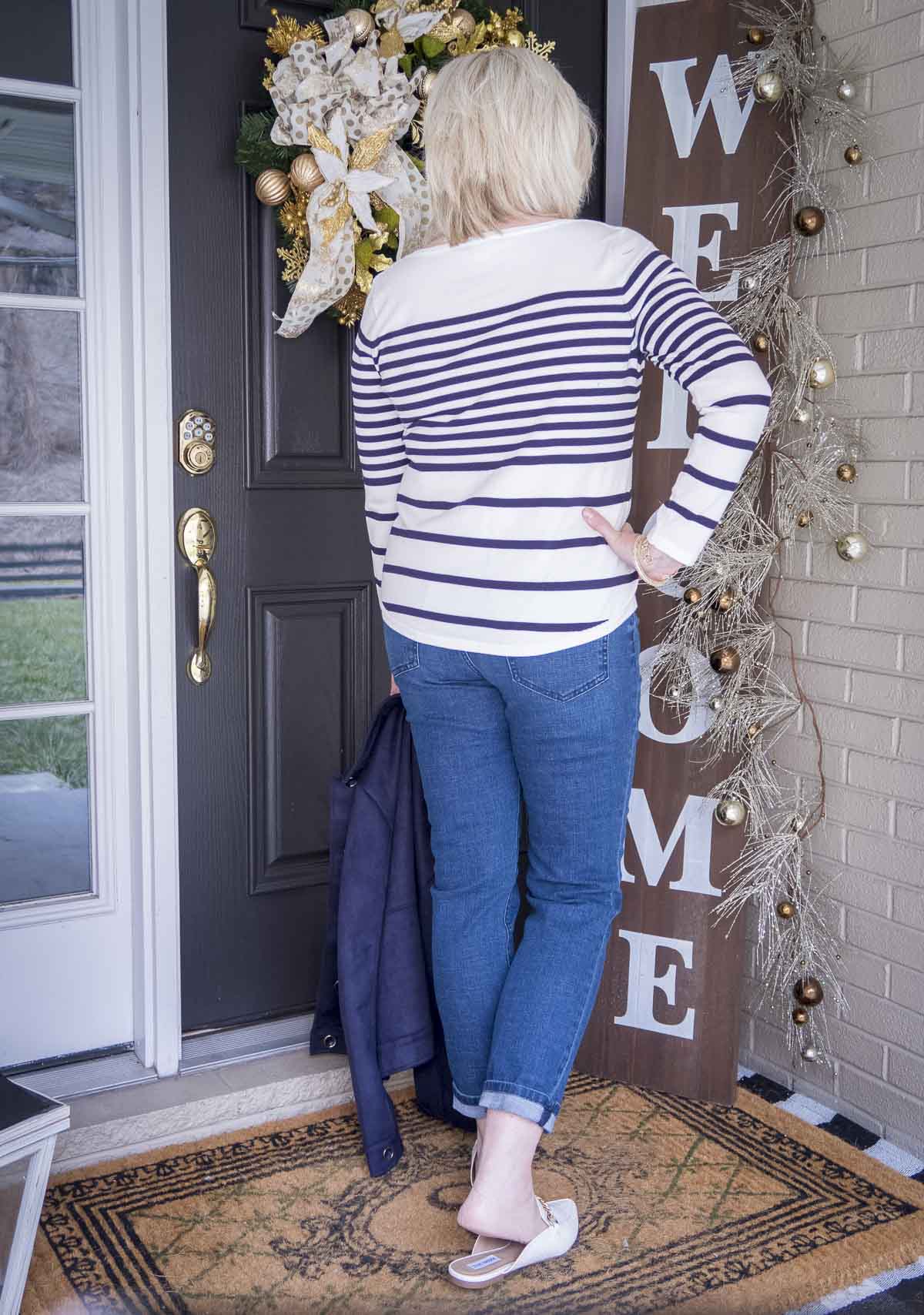 Fashion Blogger 50 Is Not Old is showing the back of a striped sweater and medium wash jeans and bone chain link mules