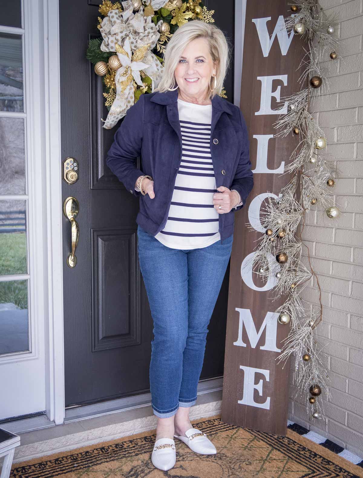Fashion Blogger 50 Is Not Old is wearing a striped sweater with a navy faux suede jacket, medium wash jeans and bone chain link mules