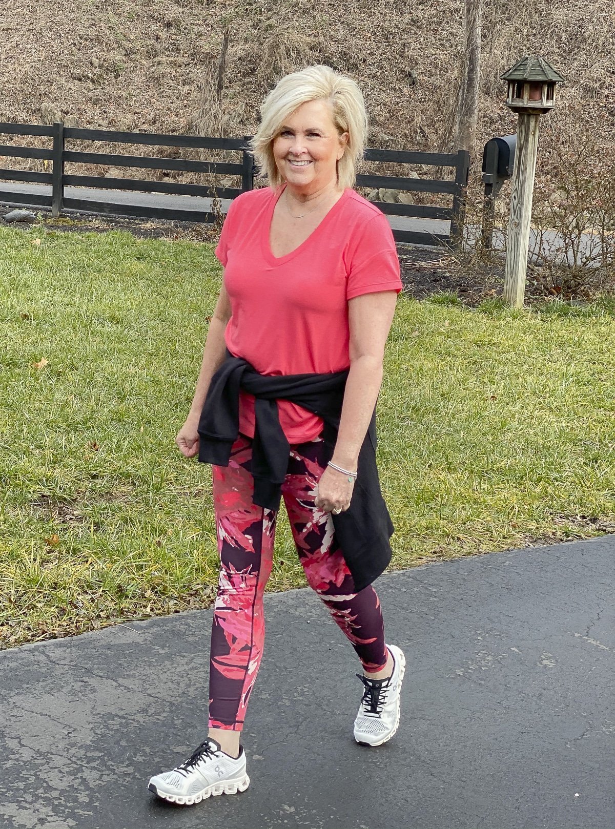 Fashion Blogger 50 Is Not Old has a black jacket tied around her waist and is wearing a pink top with printed leggings, and going walking in a pair of On Cloud training shoes