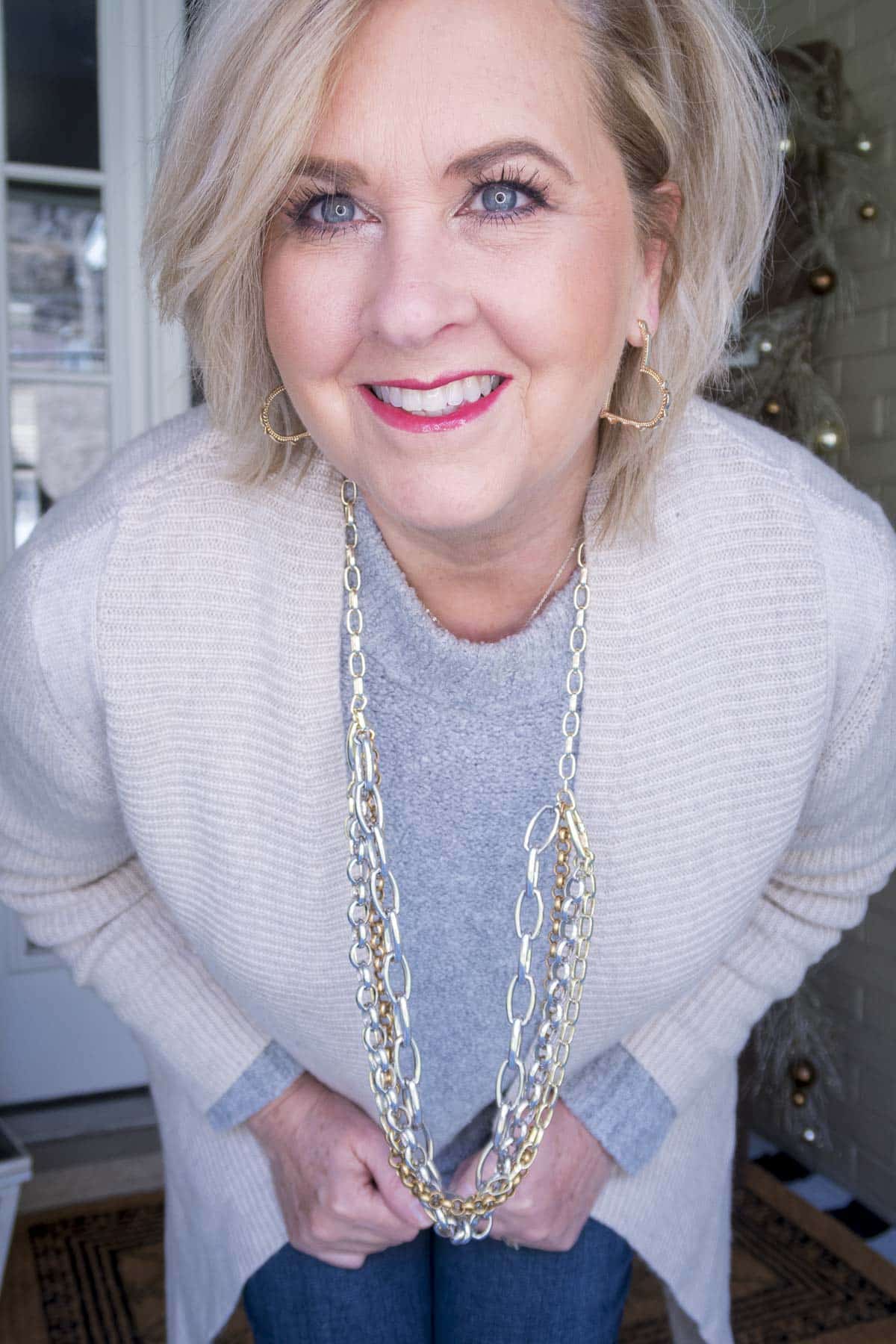 Fashion Blogger 50 Is Not Old is showing an up close look of a gray crewneck sweater, a long beige cashmere blend cardigan, and a statement necklace by Kendra Scott