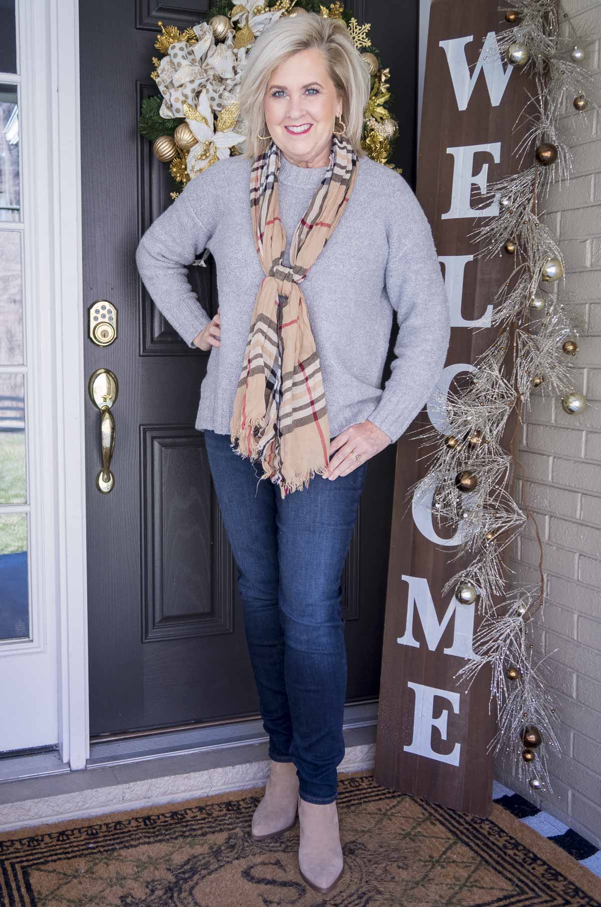 Fashion Blogger 50 Is Not Old is wearing a gray crewneck sweater, a plaid scarf, skinny jeggings, and pointy toe ankle booties