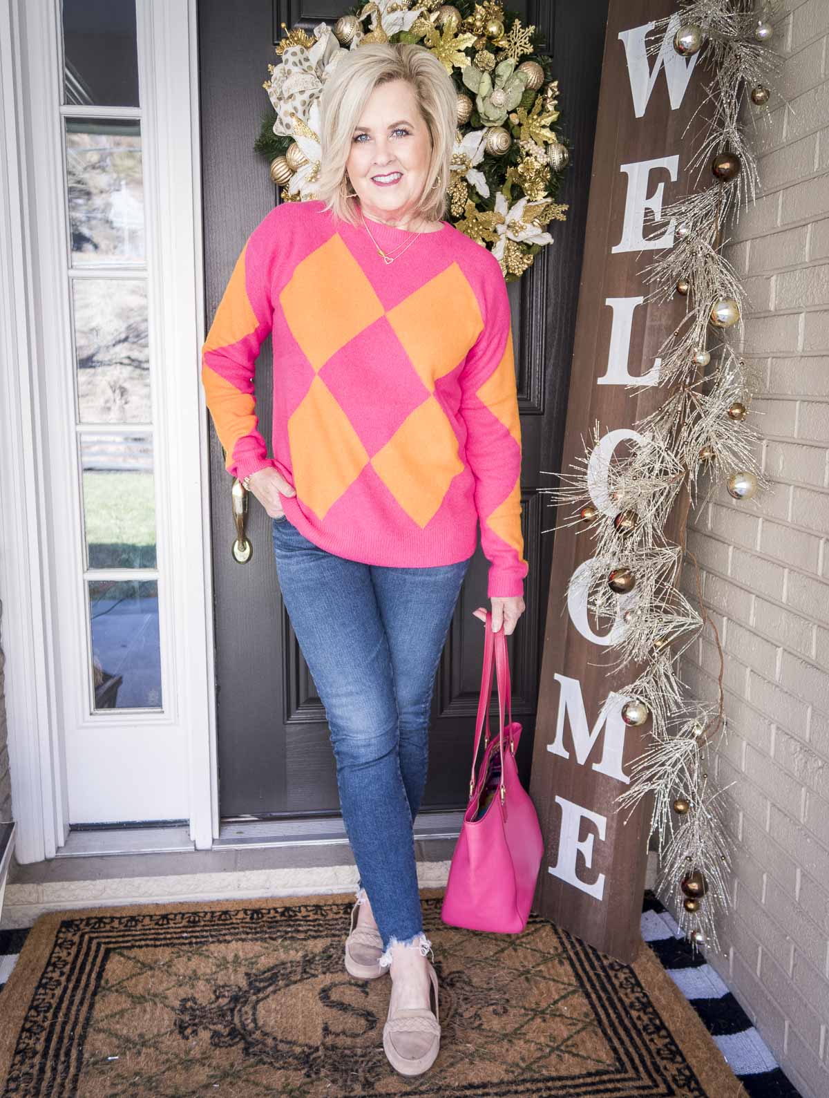 Over 40 Fashion Blogger, 50 Is Not Old is styling a bright pink and orange sweater, chewed hem skinny jeans, and neutral loafers