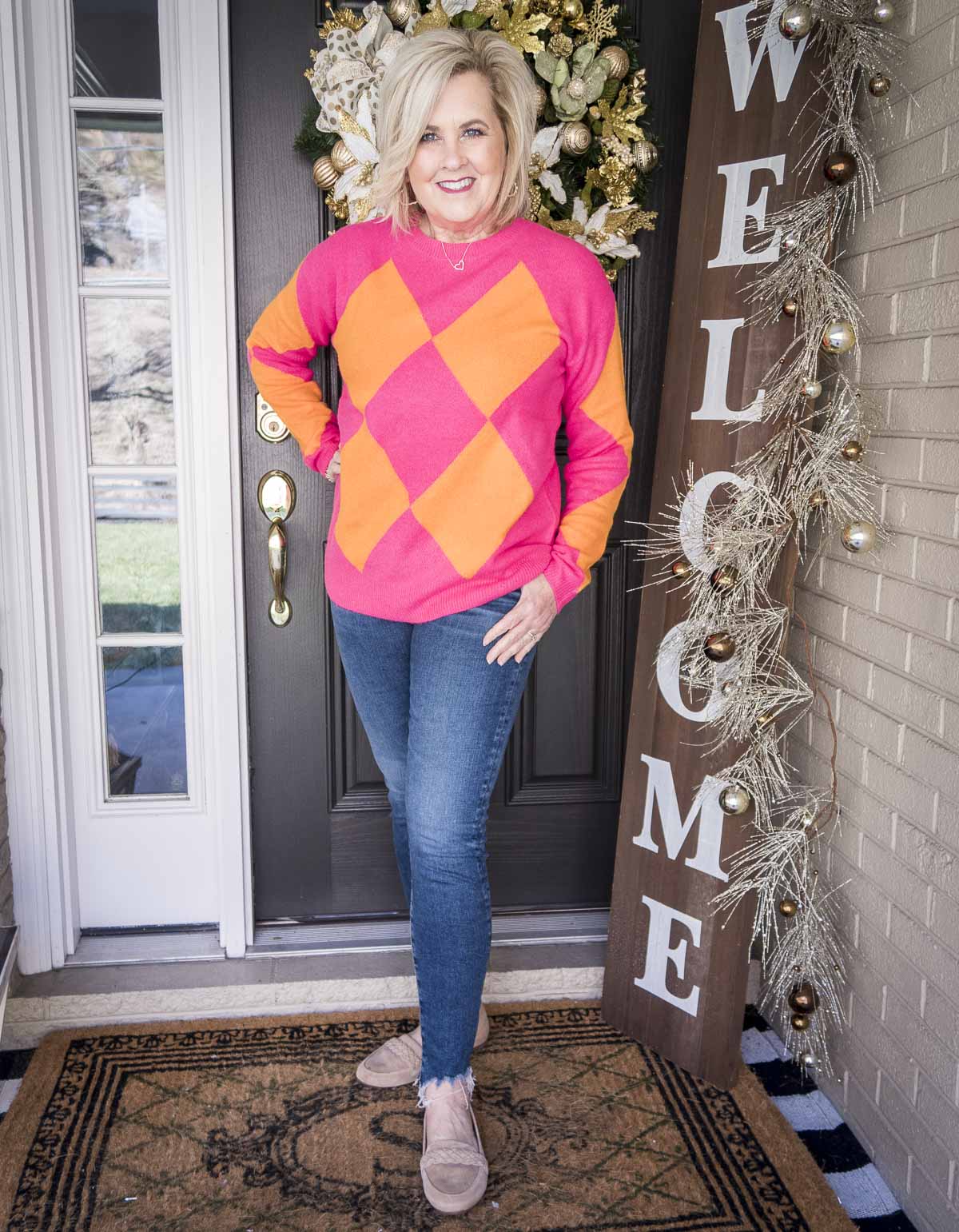 Over 40 Fashion Blogger, 50 Is Not Old is styling a pink and orange sweater, chewed hem skinny jeans, and neutral loafers