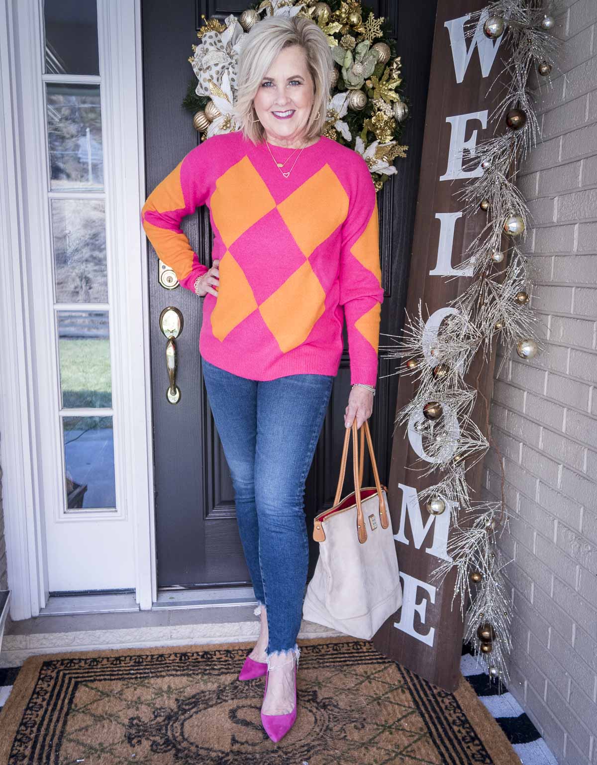 Over 40 Fashion Blogger, 50 Is Not Old is styling a bright pink and orange argyle sweater, chewed hem skinny jeans, and pink pumps