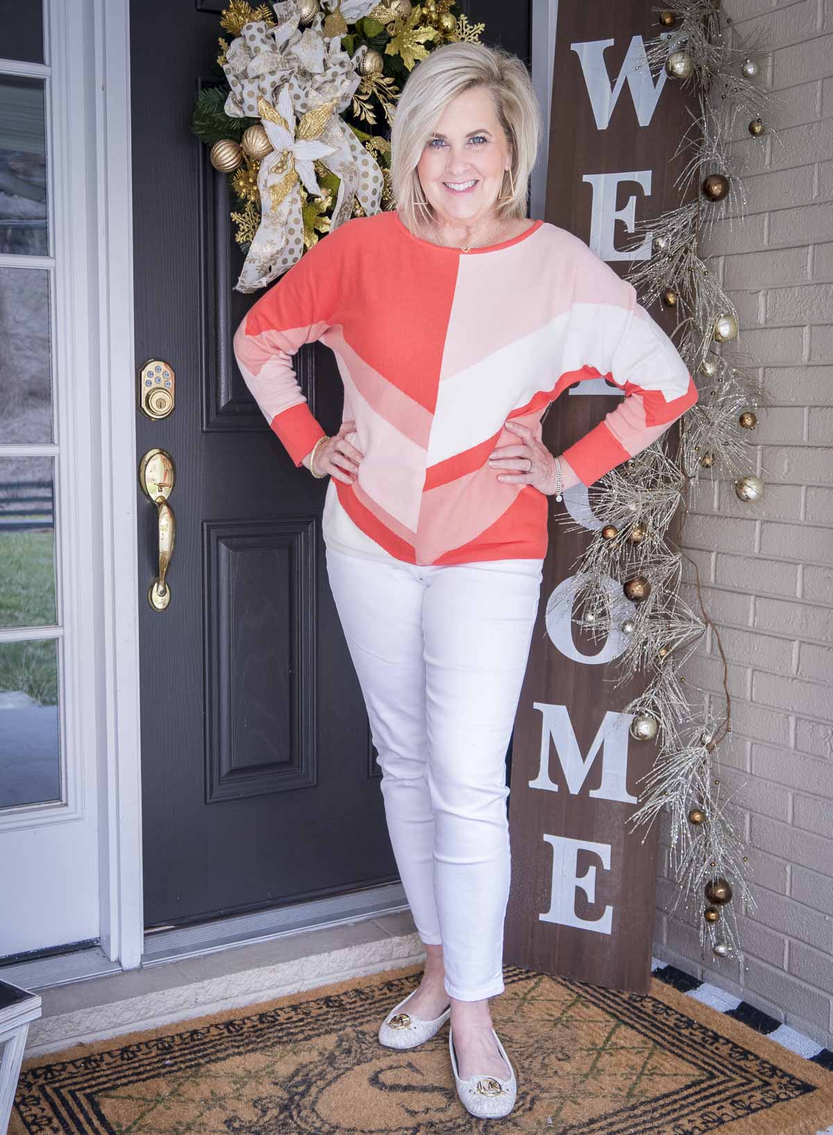 Fashion Blogger 50 Is Not Old is sporting a new haircut and a coral colorblock sweater, white ankle jeans, and white ballet flats for spring