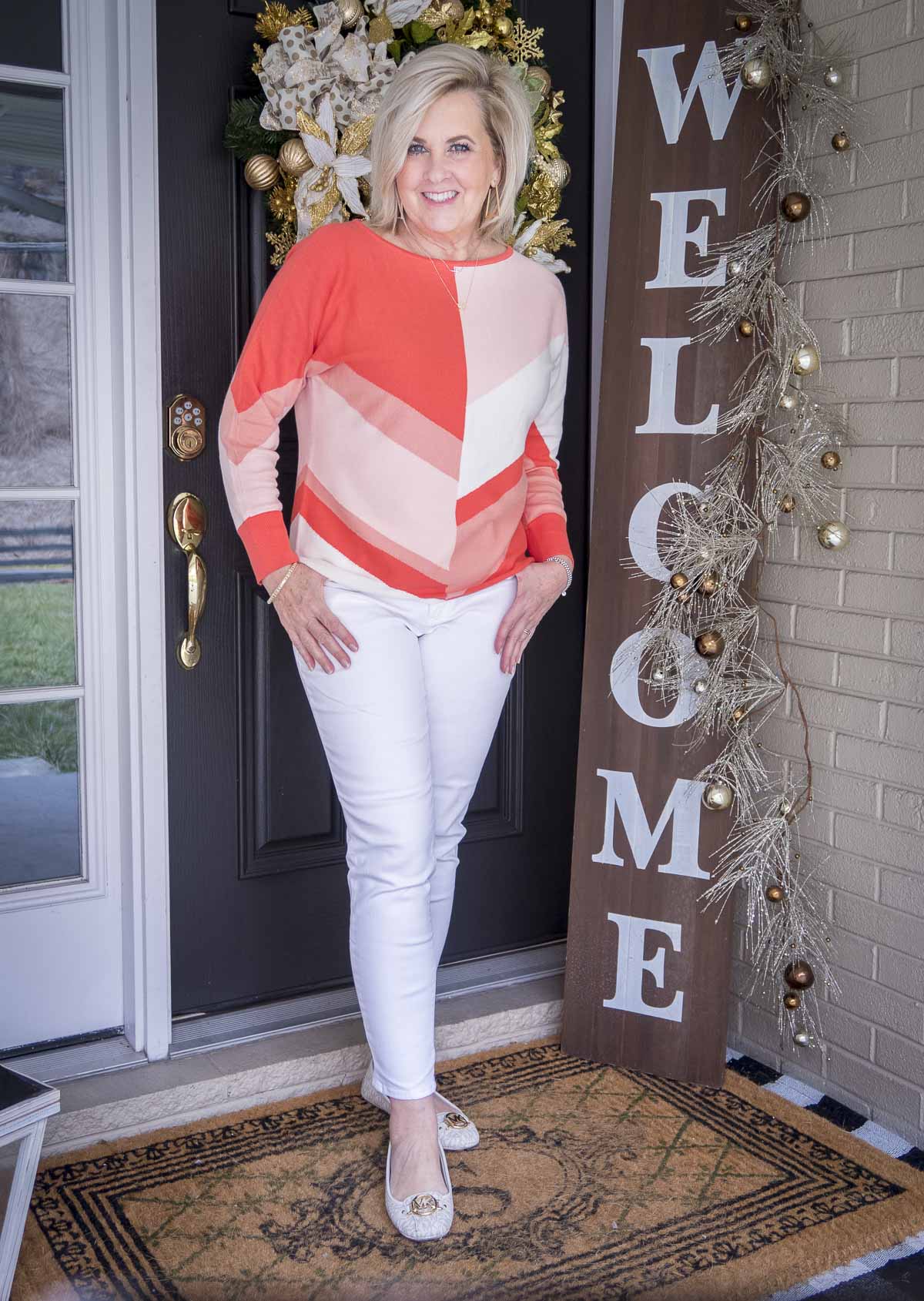 Fashion Blogger 50 Is Not Old is wearing a coral colorblock sweater, white ankle jeans, and white flats