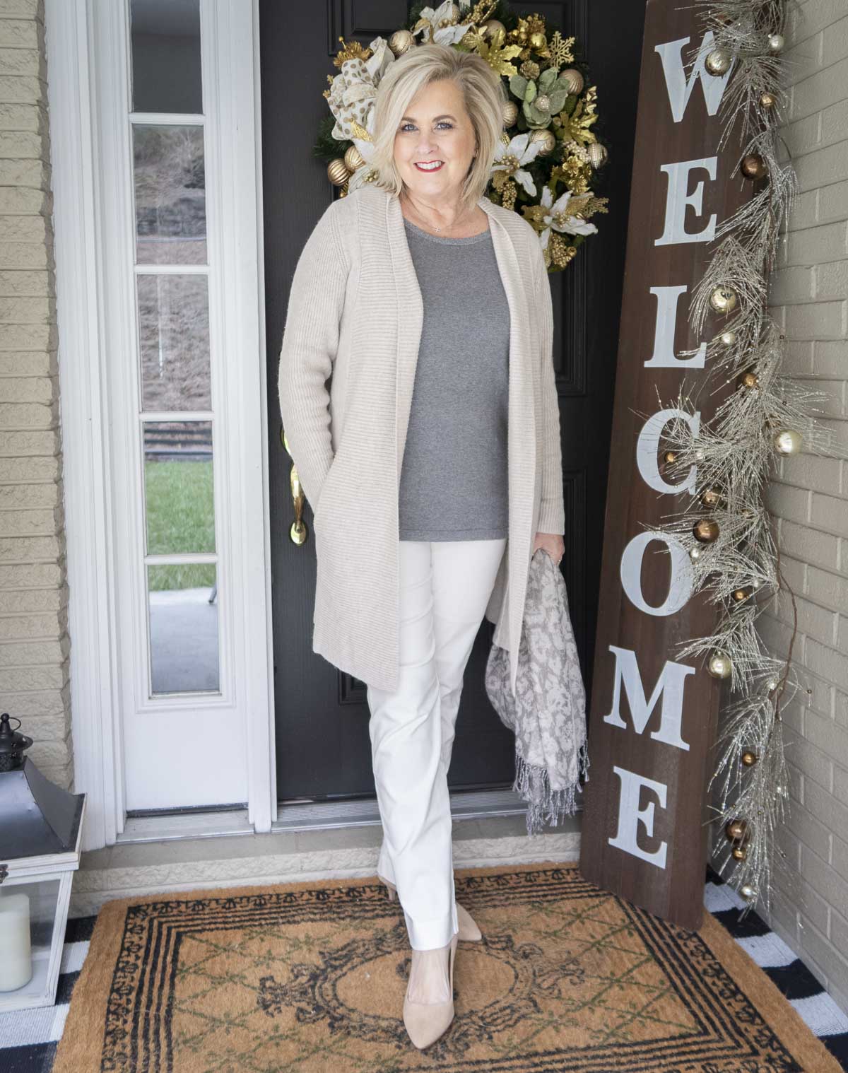 Fashion Blogger 50 Is Not Old is layering her outfit with an animal print scarf, and a long beige cardigan over a gray tank top and white pants
