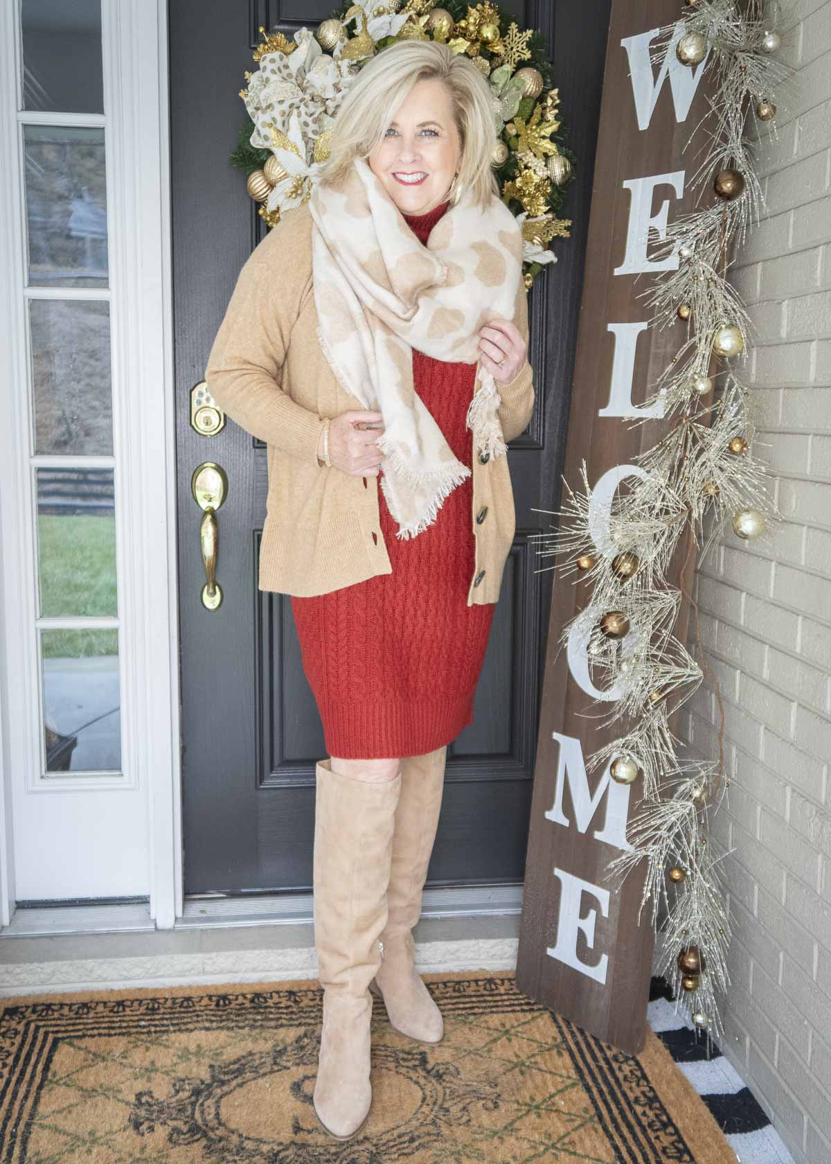 Fashion Blogger 50 Is Not Old is looking warm and cozy in a red sweater dress, animal print blanket scarf, camel cardigan, and tall boots