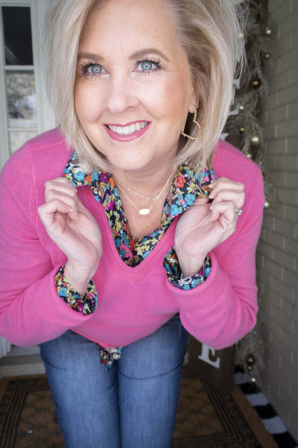 Fashion Blogger 50 Is Not Old is showing an up-close photo of a pink v-neck sweater over top of a brightly printed shirt