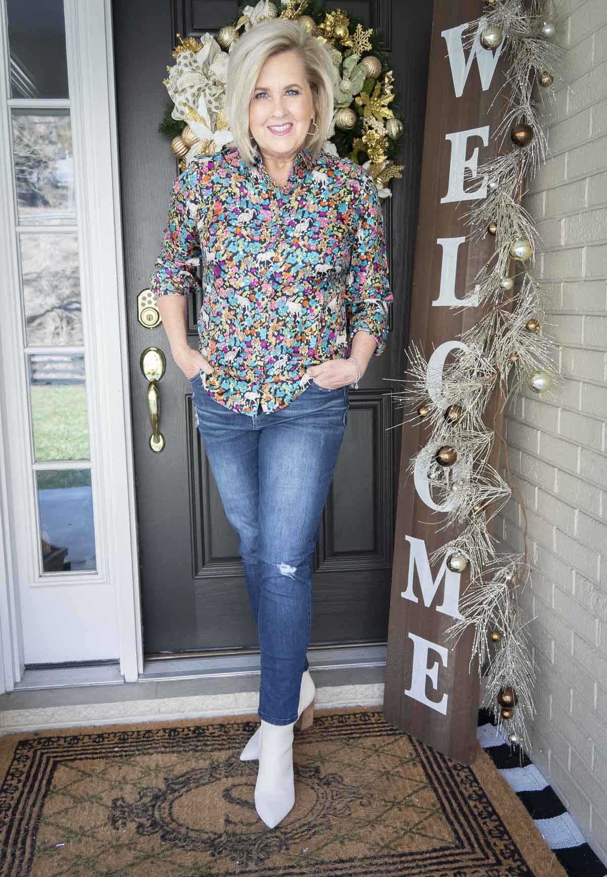 Fashion Blogger 50 Is Not Old is wearing a brightly printed shirt from J Crew, a pair of distressed skinny jeans, and a pair of white ankle boots