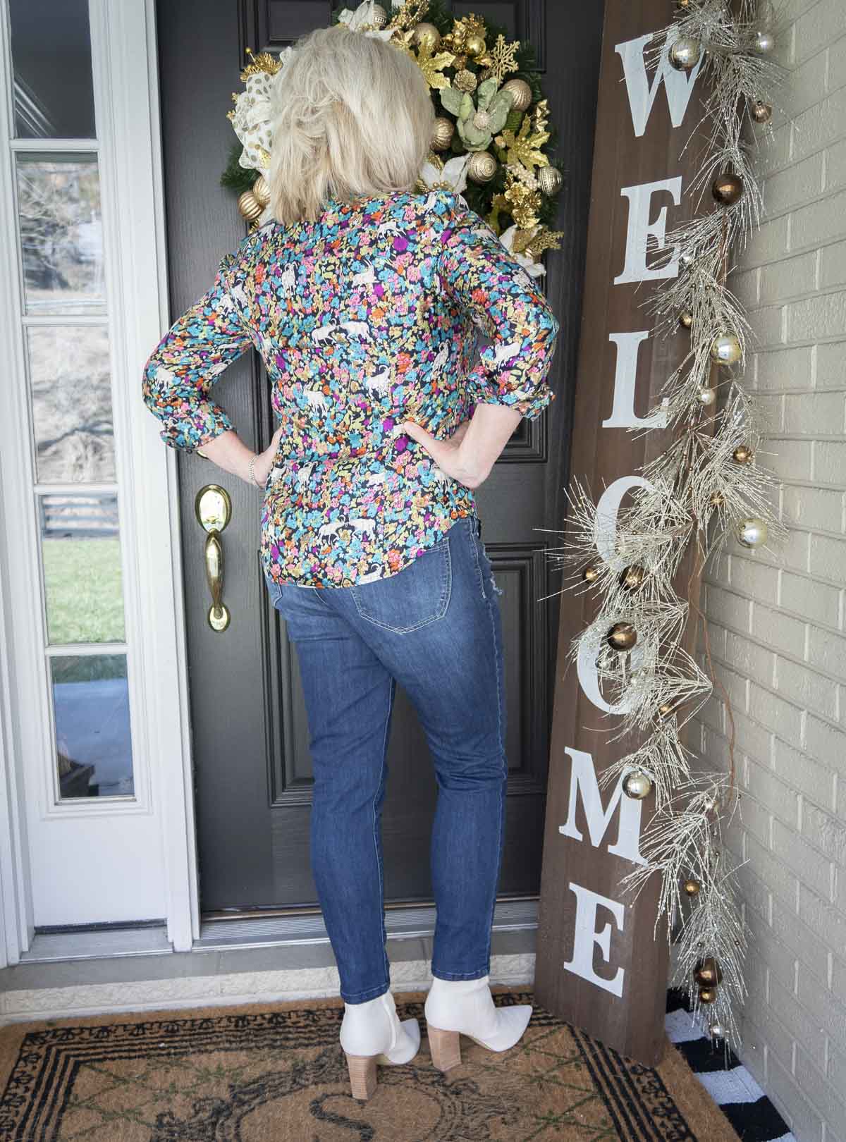 Fashion Blogger 50 Is Not Old is showing the back of a brightly printed shirt, and pair of distressed skinny jeans, and a pair of white ankle boots