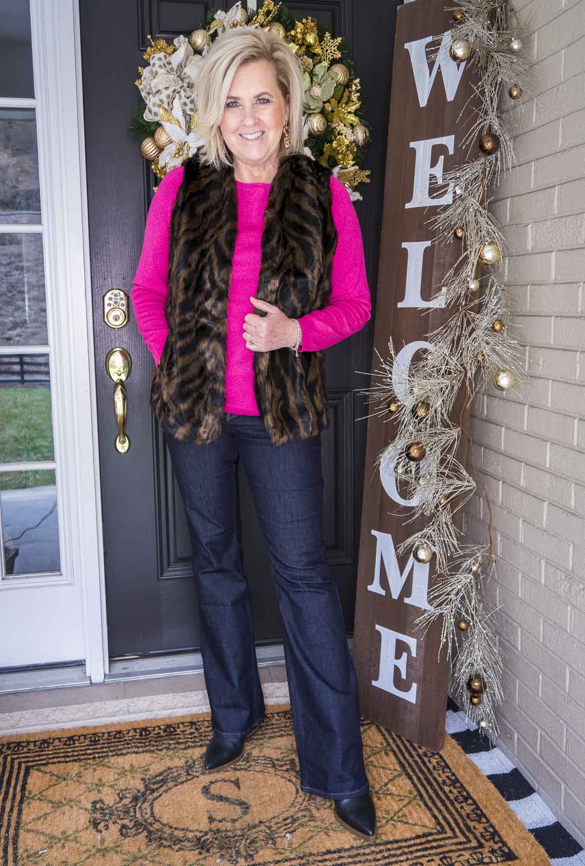 Over 40 Fashion Blogger 50 Is Not Old is wearing a bright pink sweater with a tiger print faux fur vest, flare jeans, and black pointy toe boots