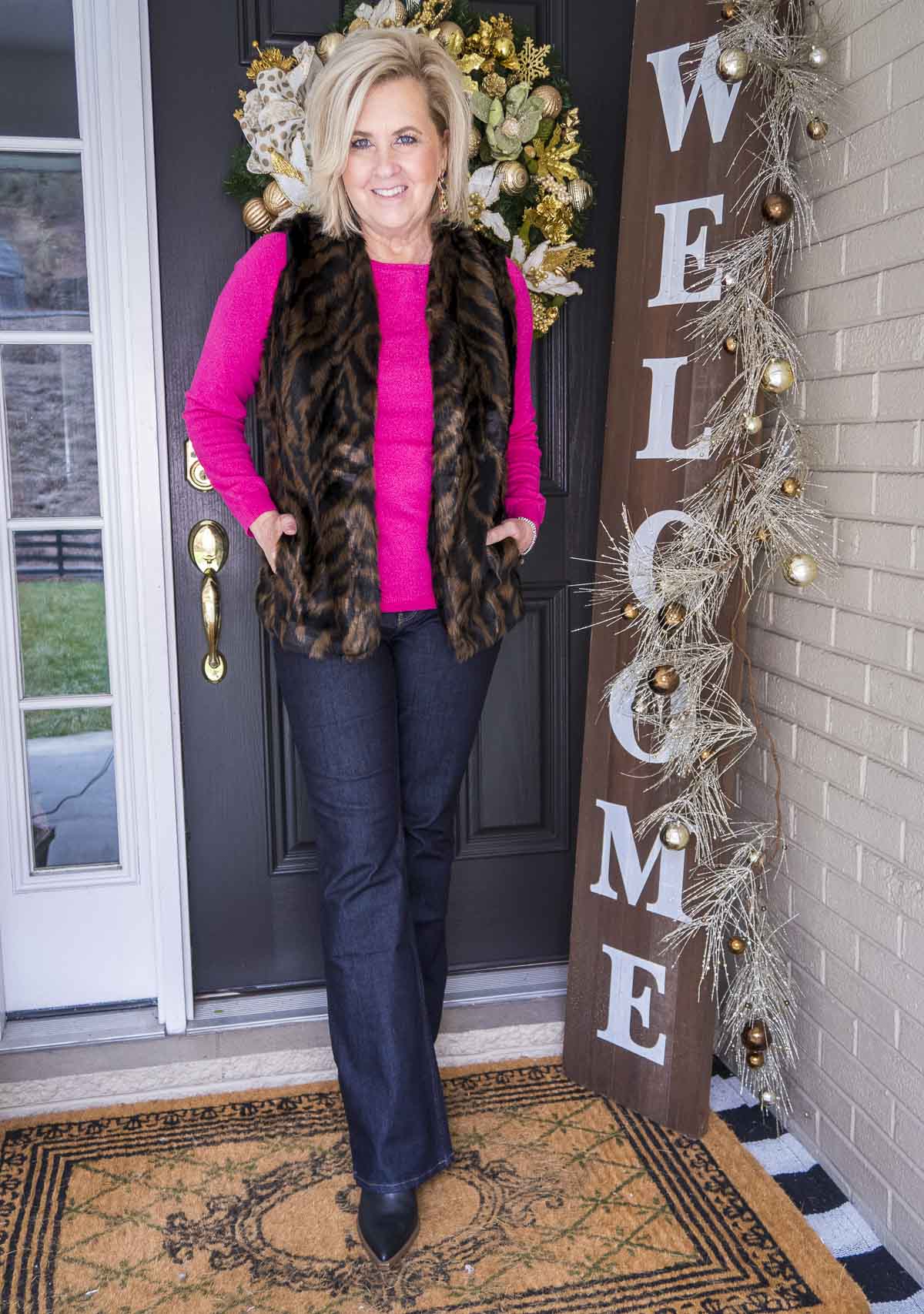 Over 40 Fashion Blogger 50 Is Not Old is wearing a bright pink sweater with a tiger print faux fur vest, flare jeans, and black pointy boots