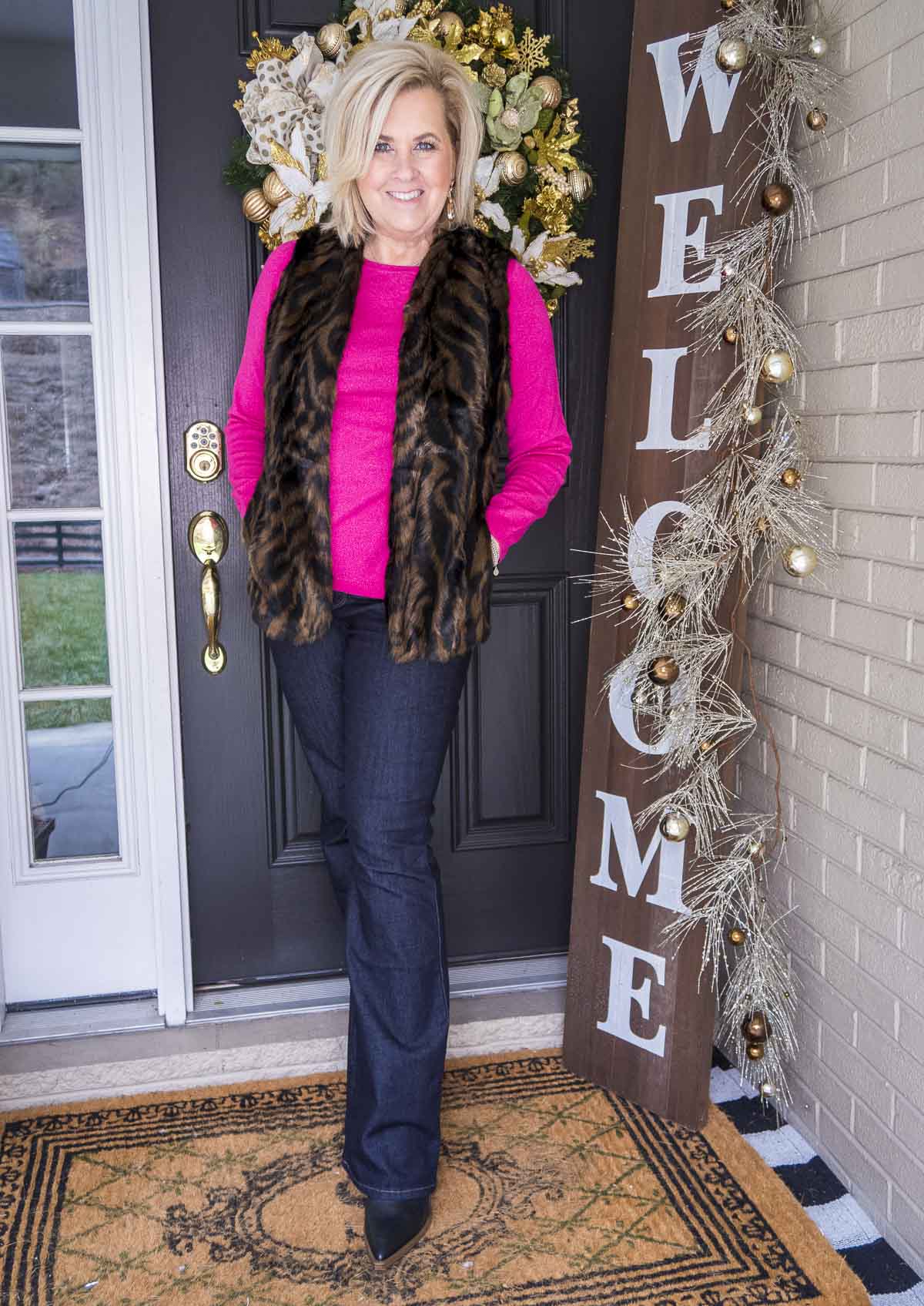 Over 40 Fashion Blogger 50 Is Not Old is wearing a bright pink sweater with a tiger print faux fur vest, flare jeans, and black boots