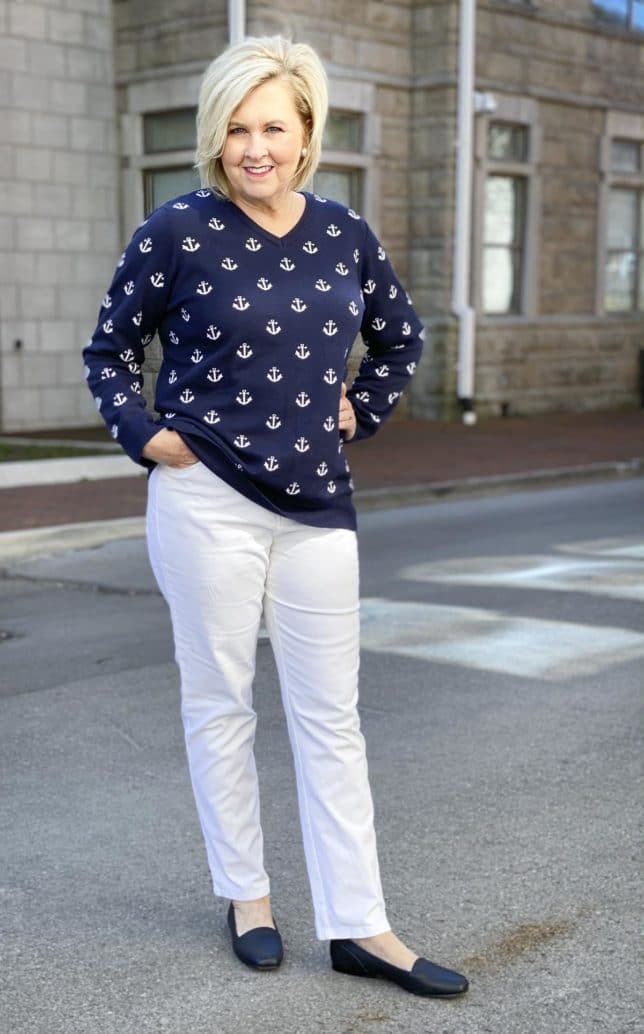 Fashion Blogger 50 Is Not Old is looking modern and stylish in this navy v-neck sweaters with white anchors, white ankle pants, and navy flats