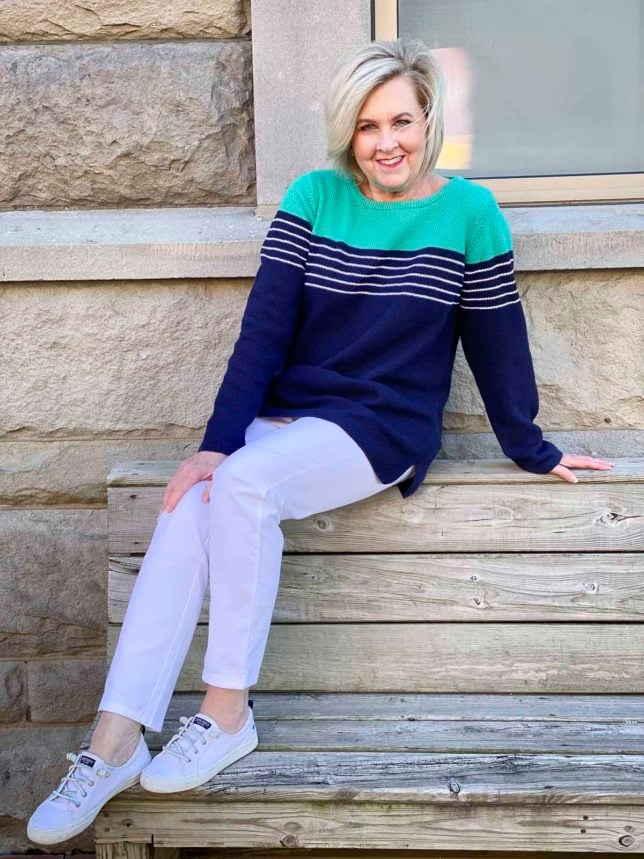 Fashion Blogger 50 Is Not Old is wearing a navy sweater with white stripes, a pair of white ankle pants, and white sneakers