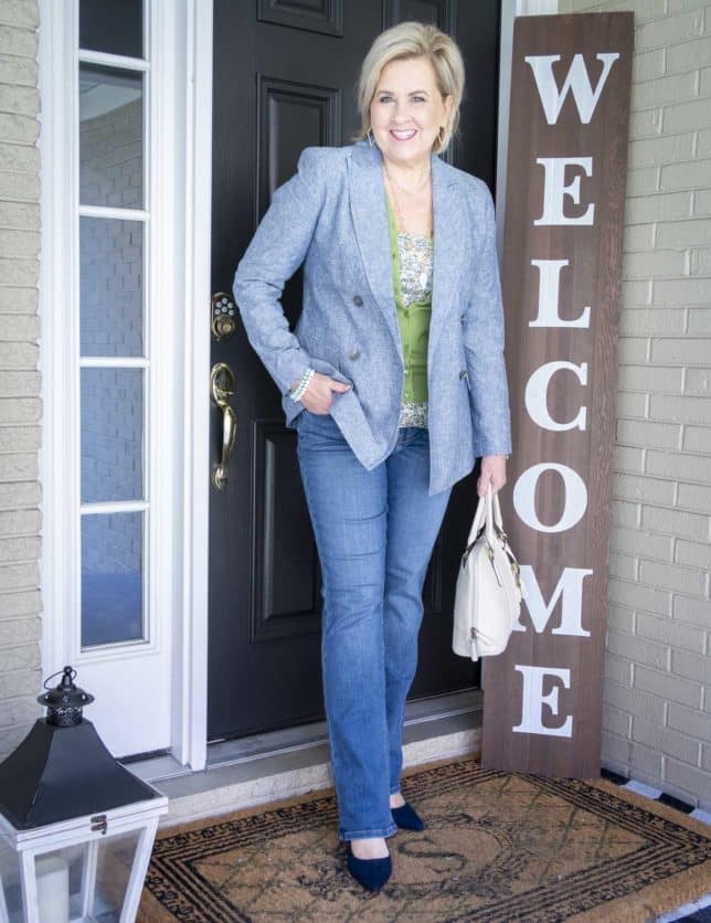 Fashion Blogger 50 Is Not Old is wearing lots of layers for Spring including a double breasted blazer, an apple green cardigan, a floral camisole, an ivory handbag, a bootcut jeans, and navy heels