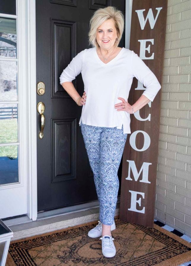 Fashion Blogger 50 Is Not Old is wearing a white v-neck tunic, a blue printed ankle pant, and white Sperry sneakers
