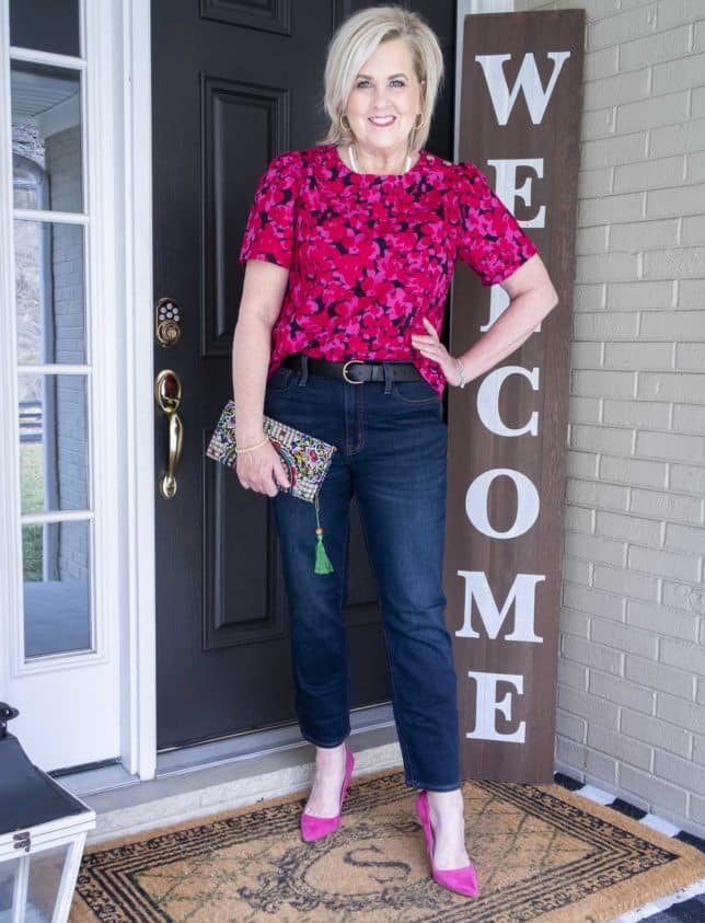 Fashion Blogger 50 Is Not Old is wearing a bright pink floral top with dark wash straight leg jeans and bright pink pumps