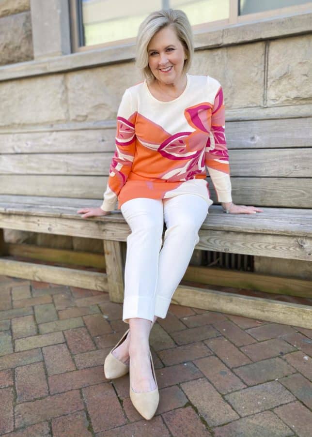 Fashion Blogger 50 Is Not Old is wearing a beautiful tunic sweater with a large floral print, ecru cuffed dress pants, and neutral kitten heels